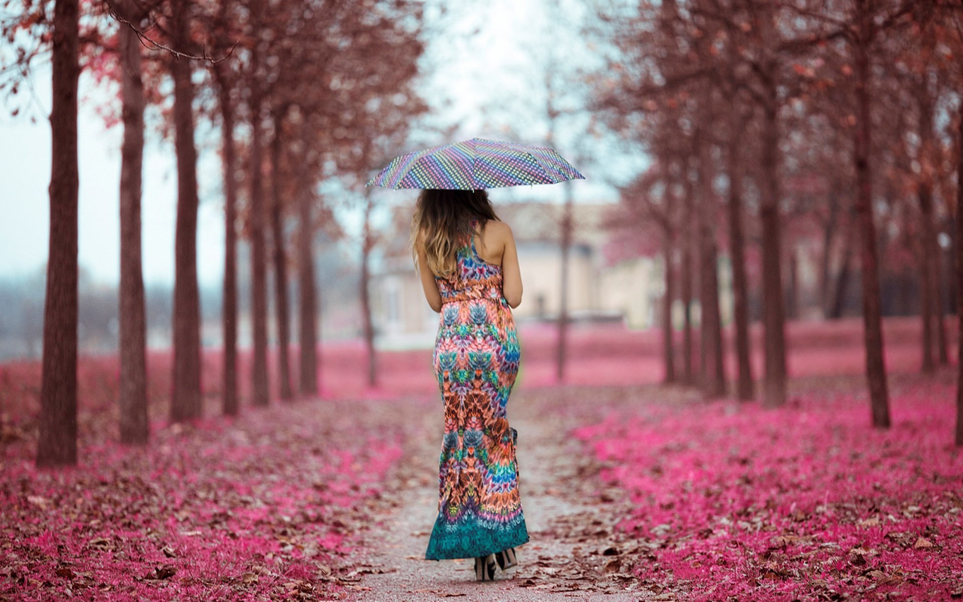 The girl under an umbrella in a beautiful dress goes through the alley