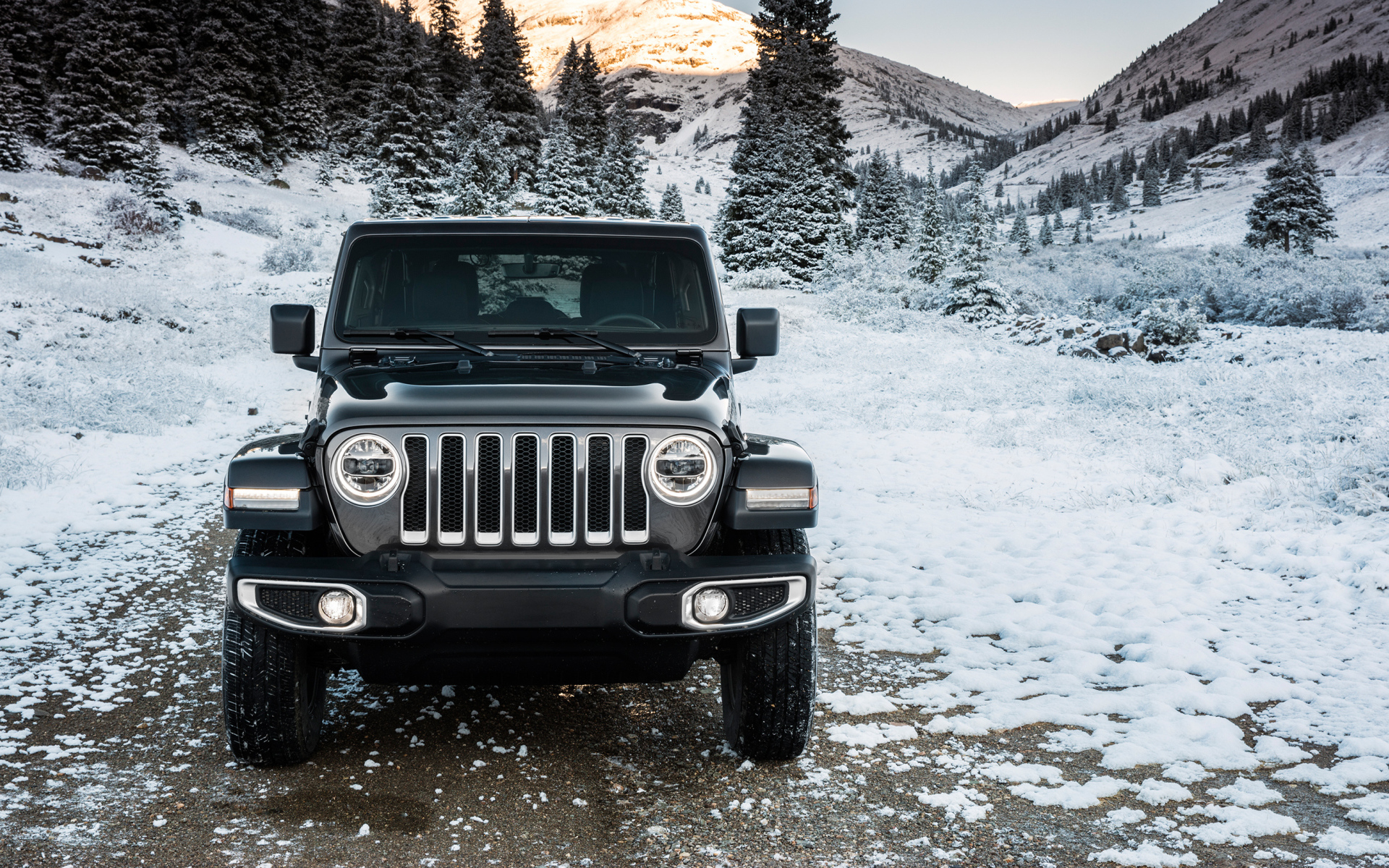 Внедорожник Jeep Wrangler Unlimited Sahara, 2018 на заснеженной дороге на фоне гор