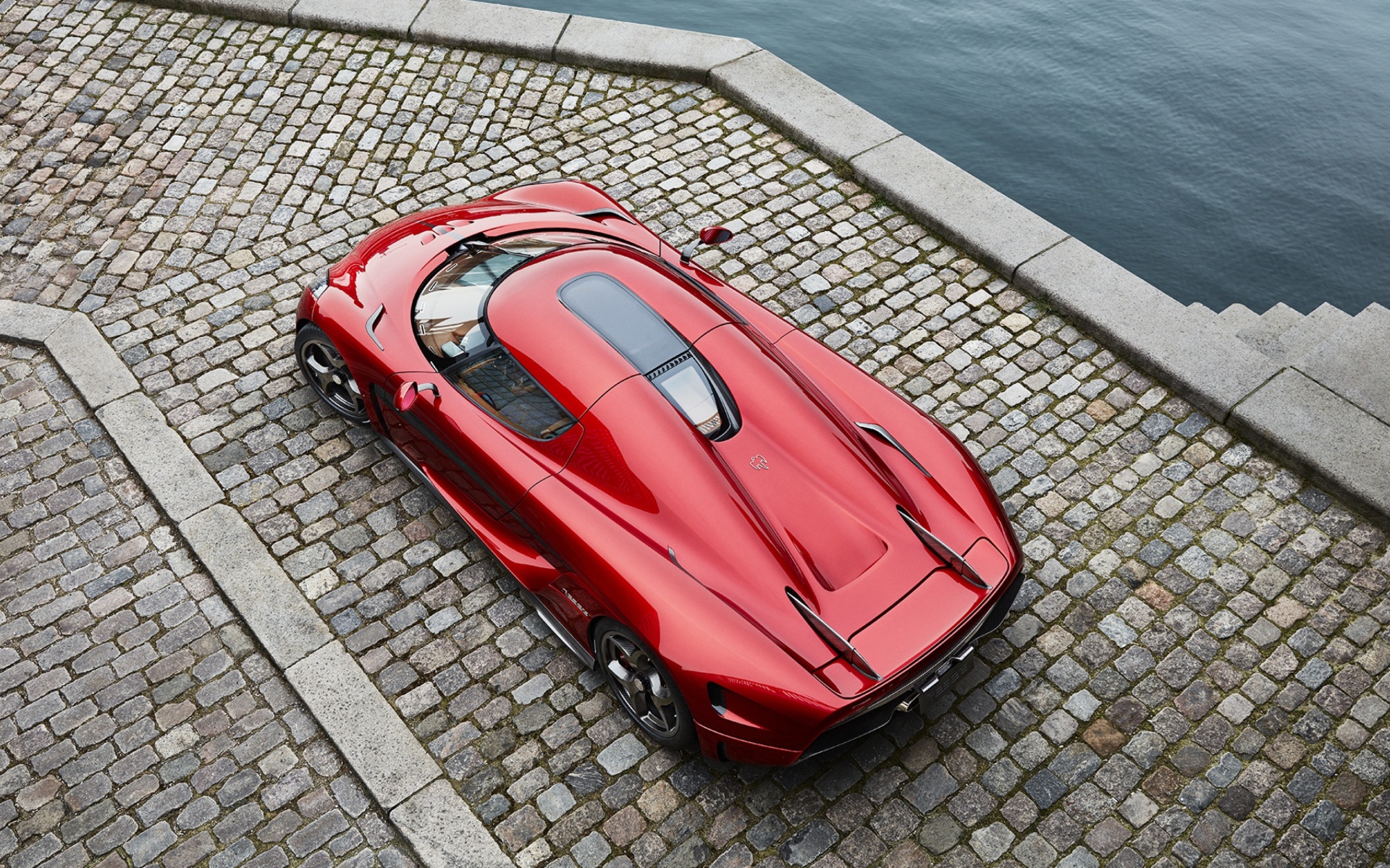 Красный спортивный автомобиль Koenigsegg Regera у воды, вид сверху