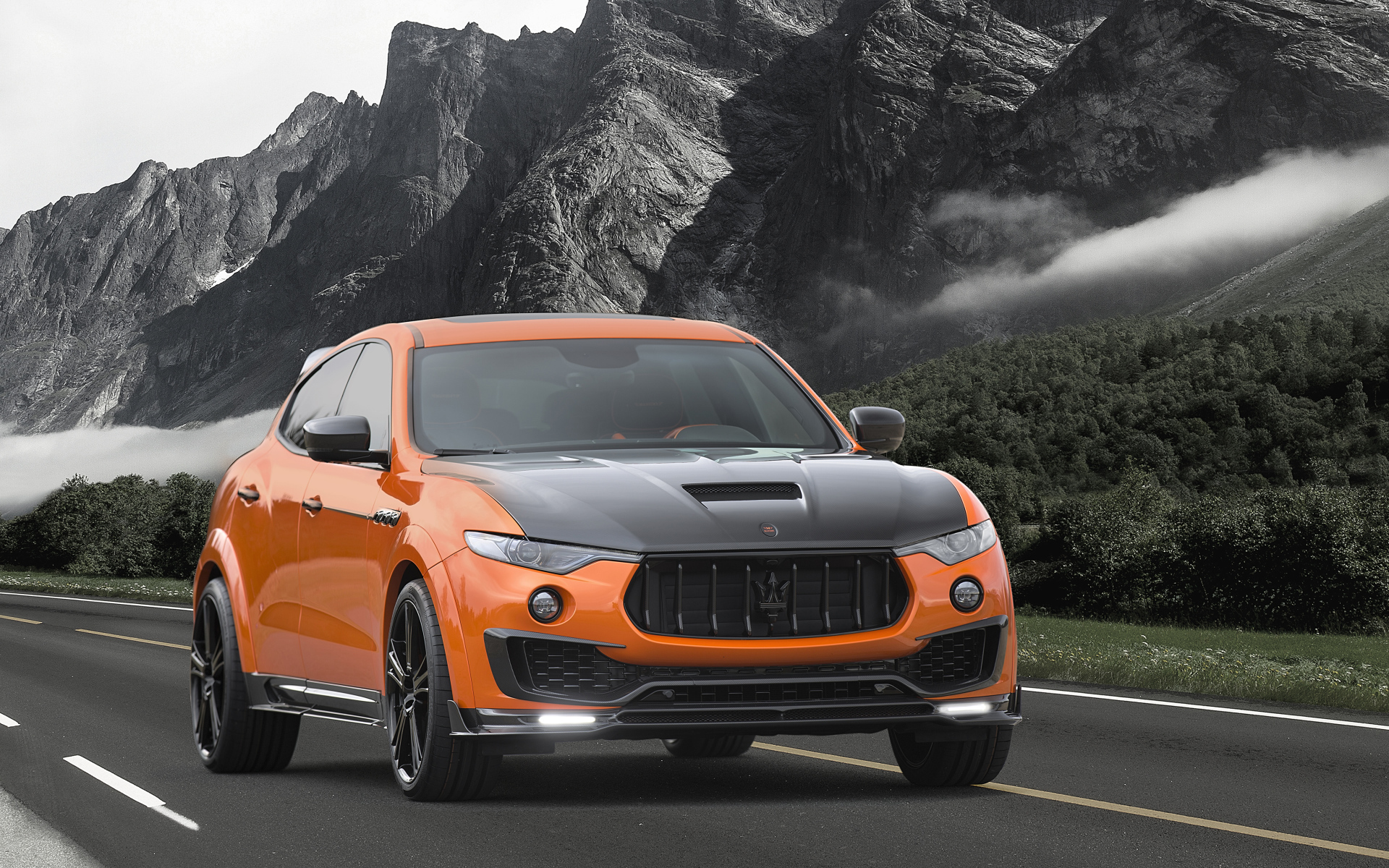 Оранжевый автомобиль Maserati Mansory Levante, 2017 на фоне гор