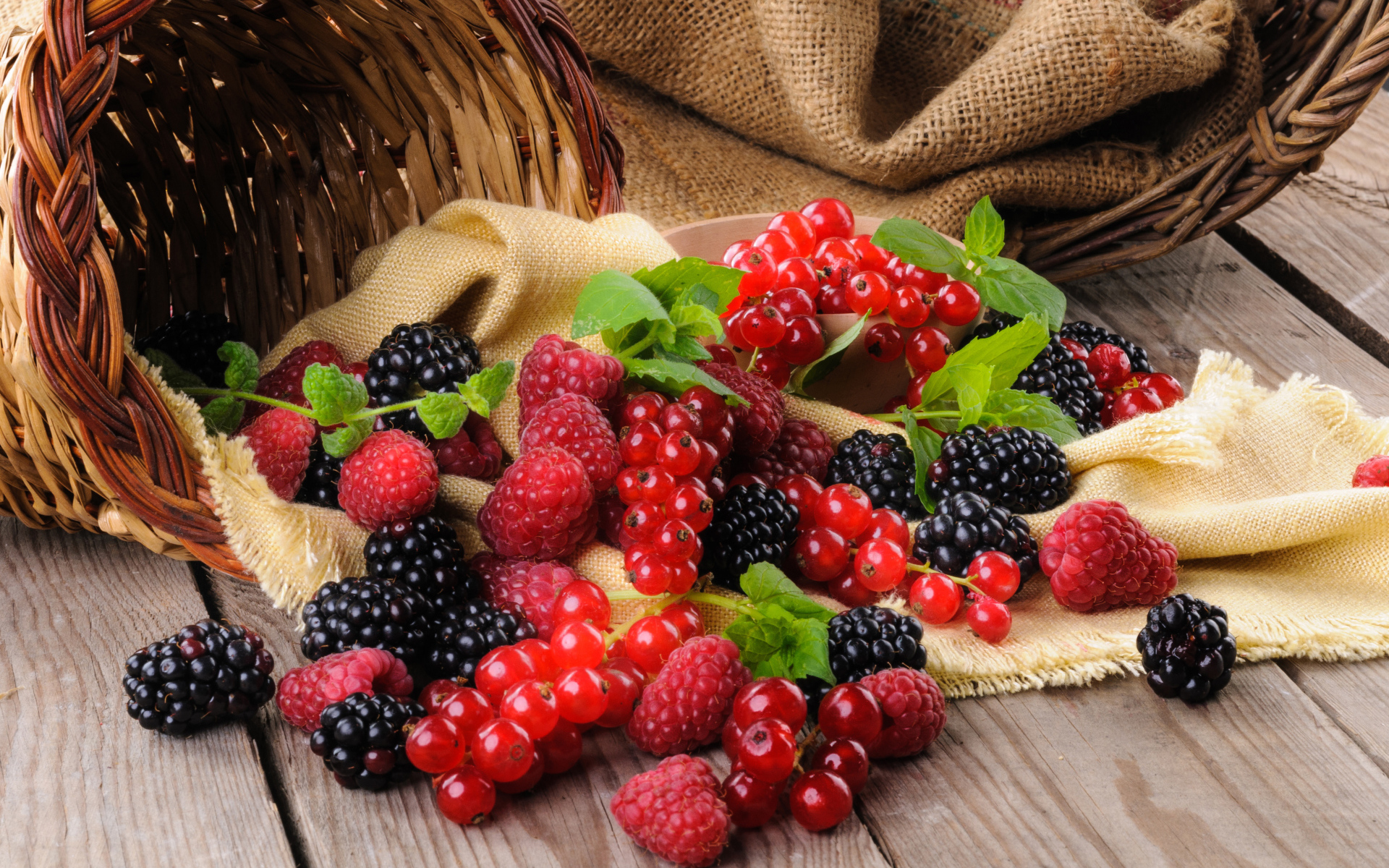 Свежие ягоды ежевики, малины и красной смородины с корзиной на столе