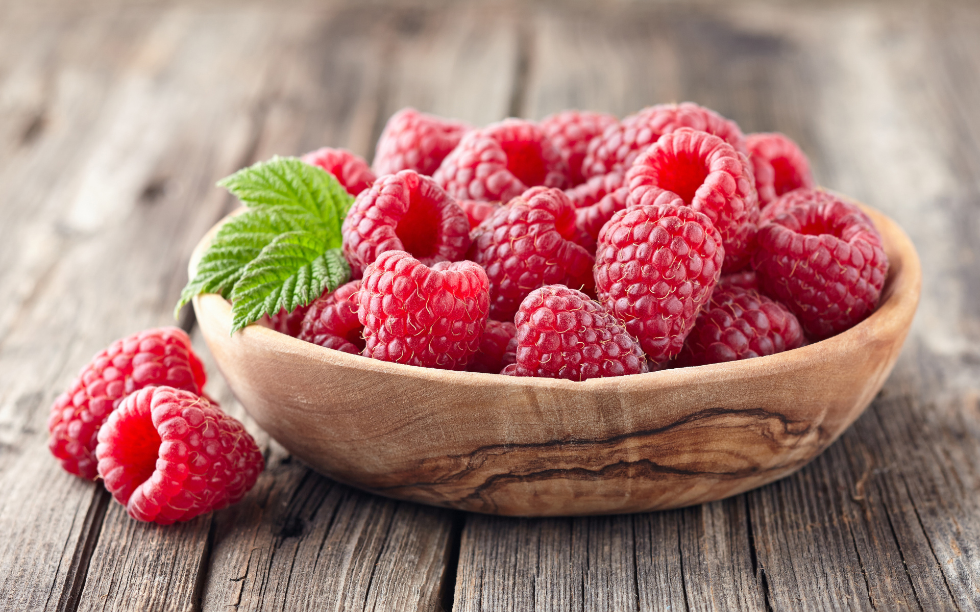 Крупные спелые ягоды малины в деревянной миске на столе