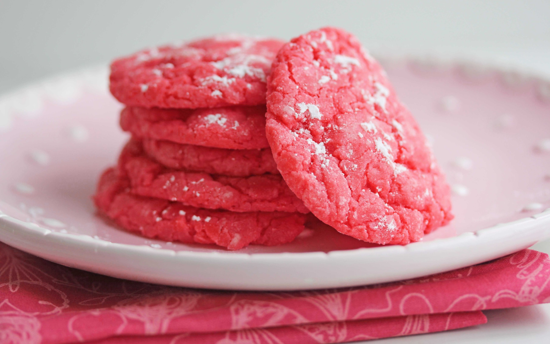 Печенье розового цвета на белой тарелке с сахарной пудрой