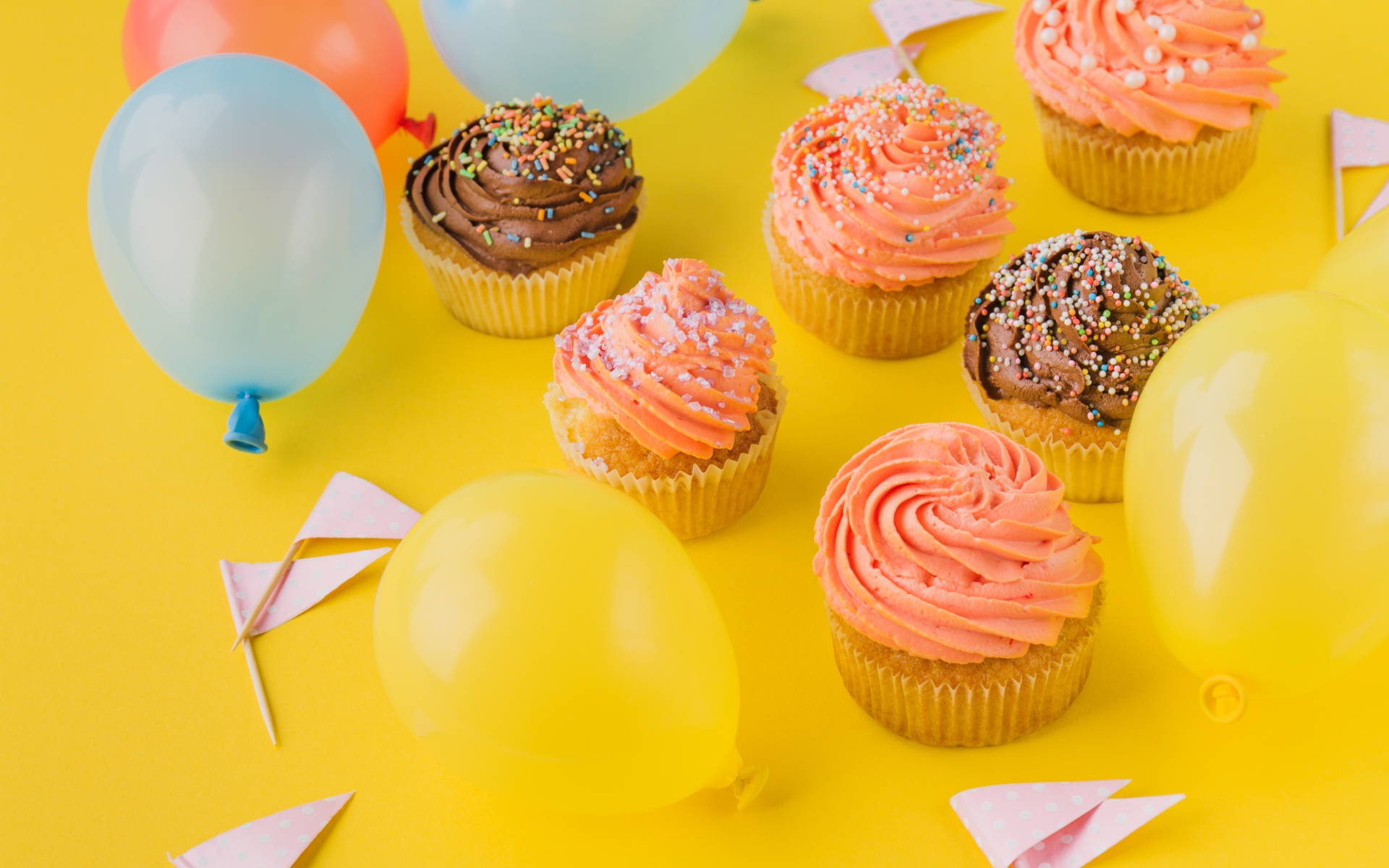 Аппетитные капкейки с кремом и воздушными шариками на желтой поверхности
