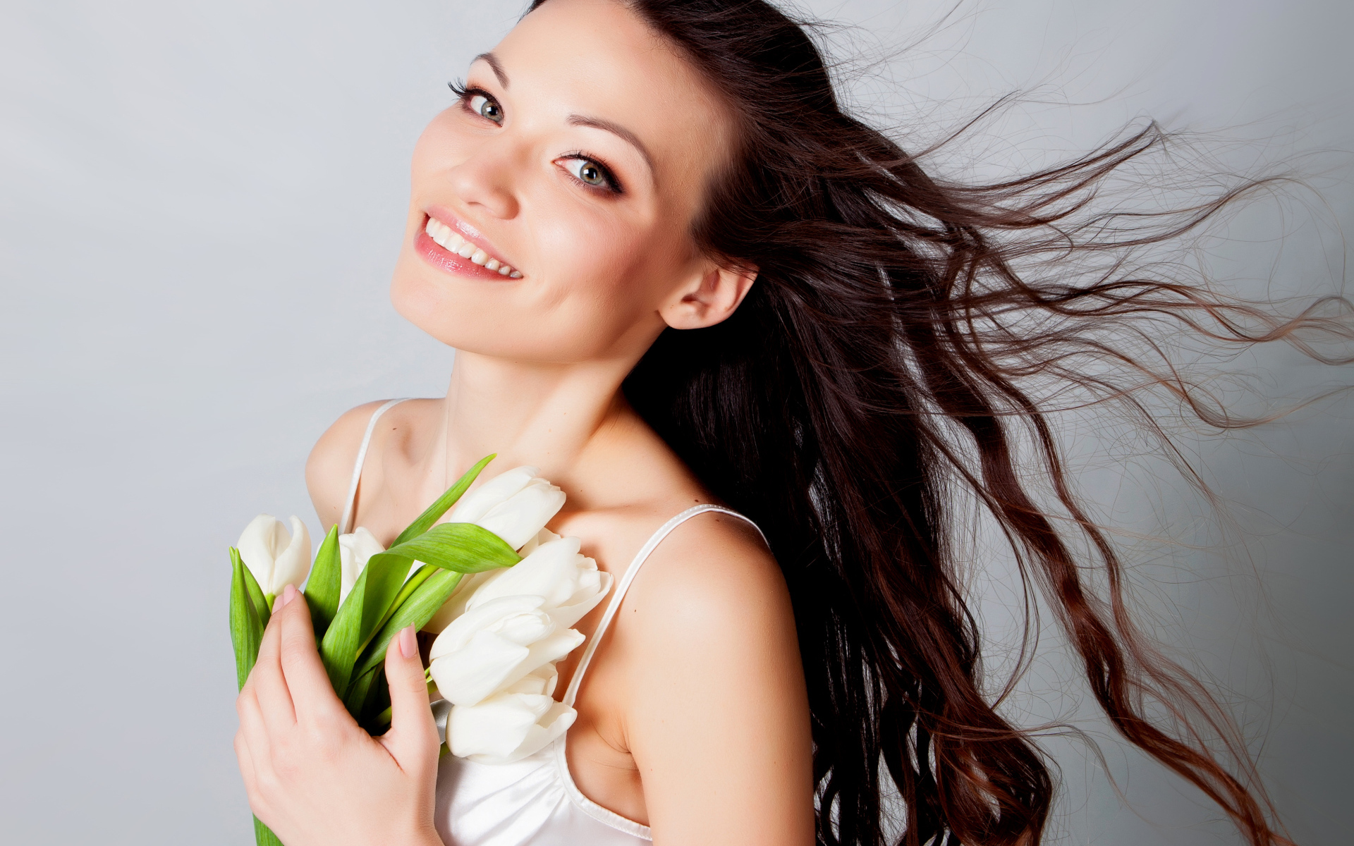 Красивая улыбающаяся брюнетка с букетом тюльпанов на сером фоне