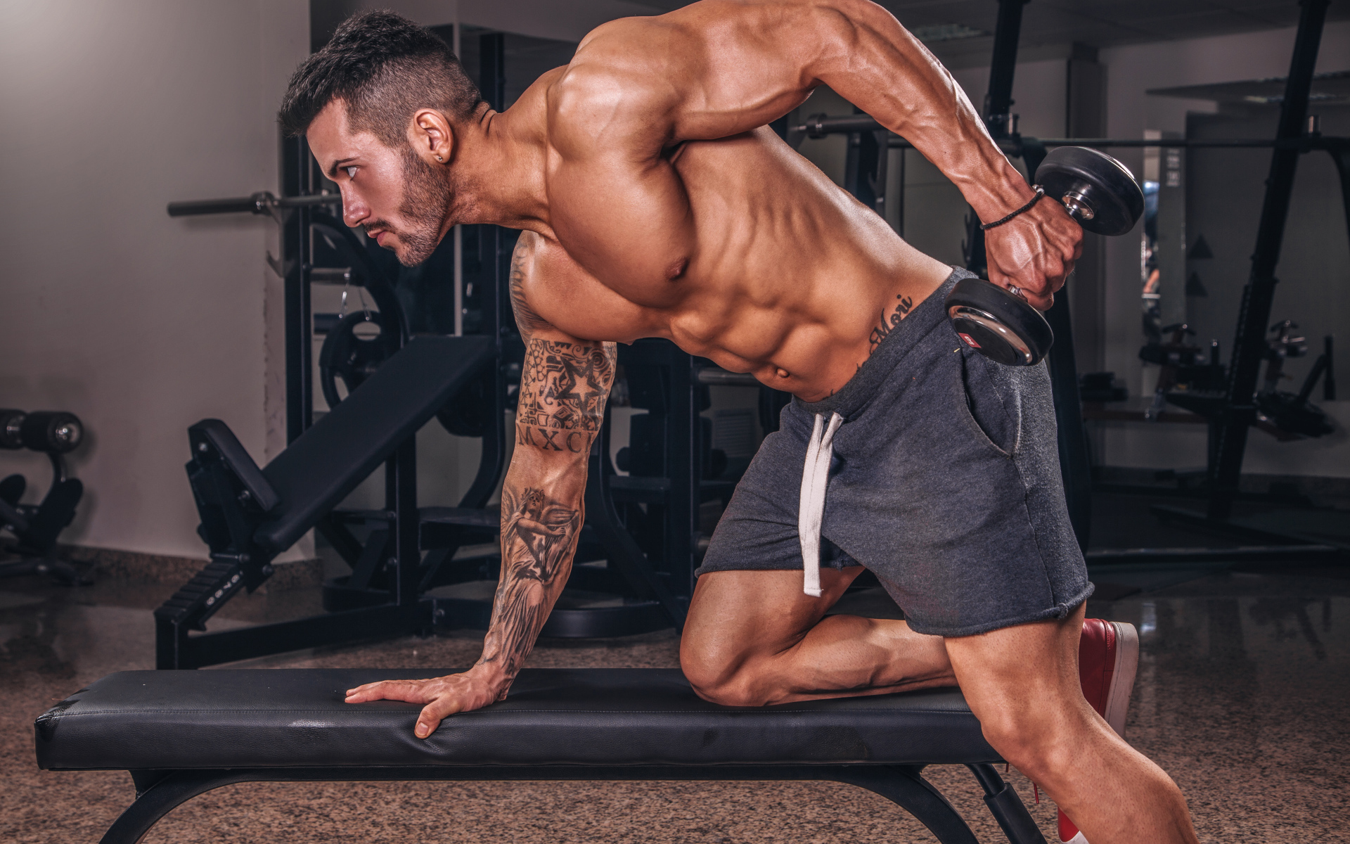 Мускулистый мужчина занимается в спортзале с гантелей