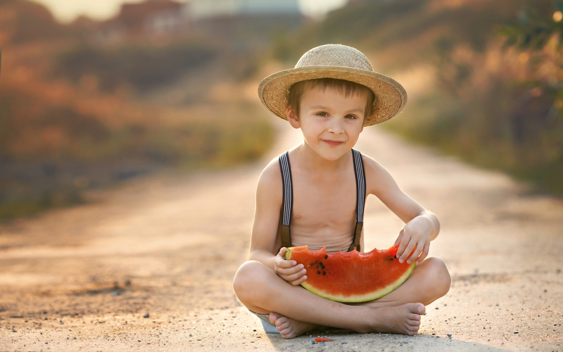 Маленький мальчик в шляпе сидит на дороге с долькой арбуза
