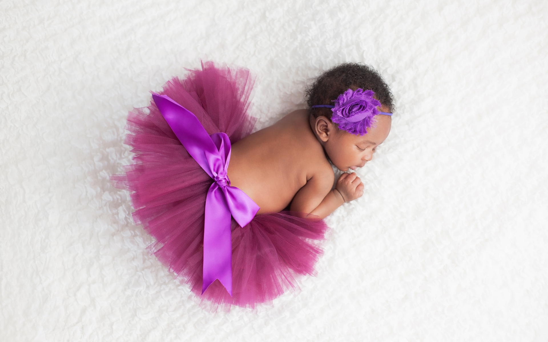 Маленькая девочка в красивой пышной юбке спит на белом покрывале