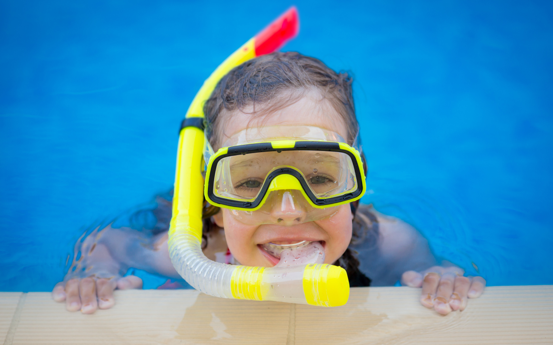 Маленькая девочка в маске с трубкой плавает в бассейне
