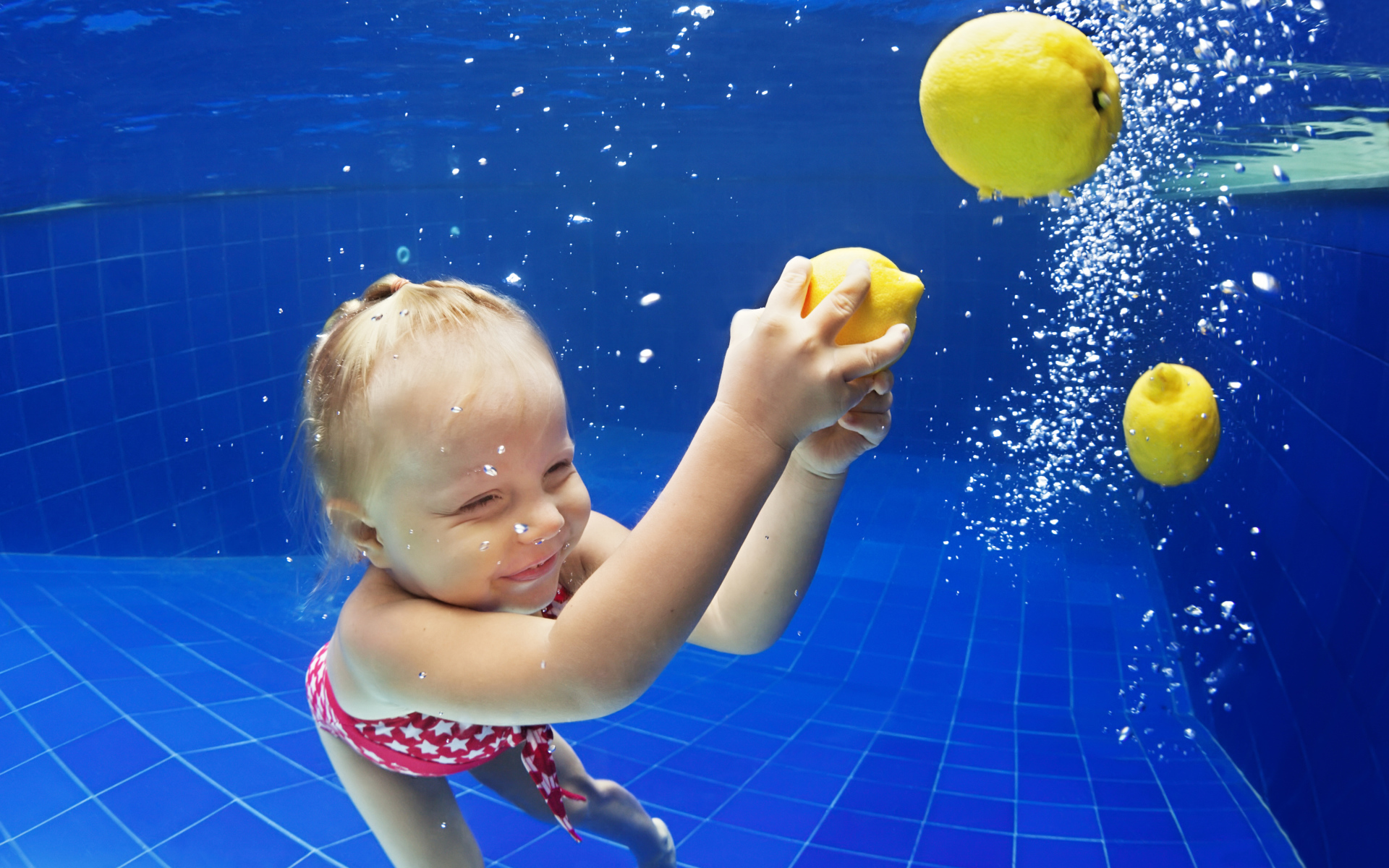 Маленькая девочка плавает в бассейне с желтыми лимонами