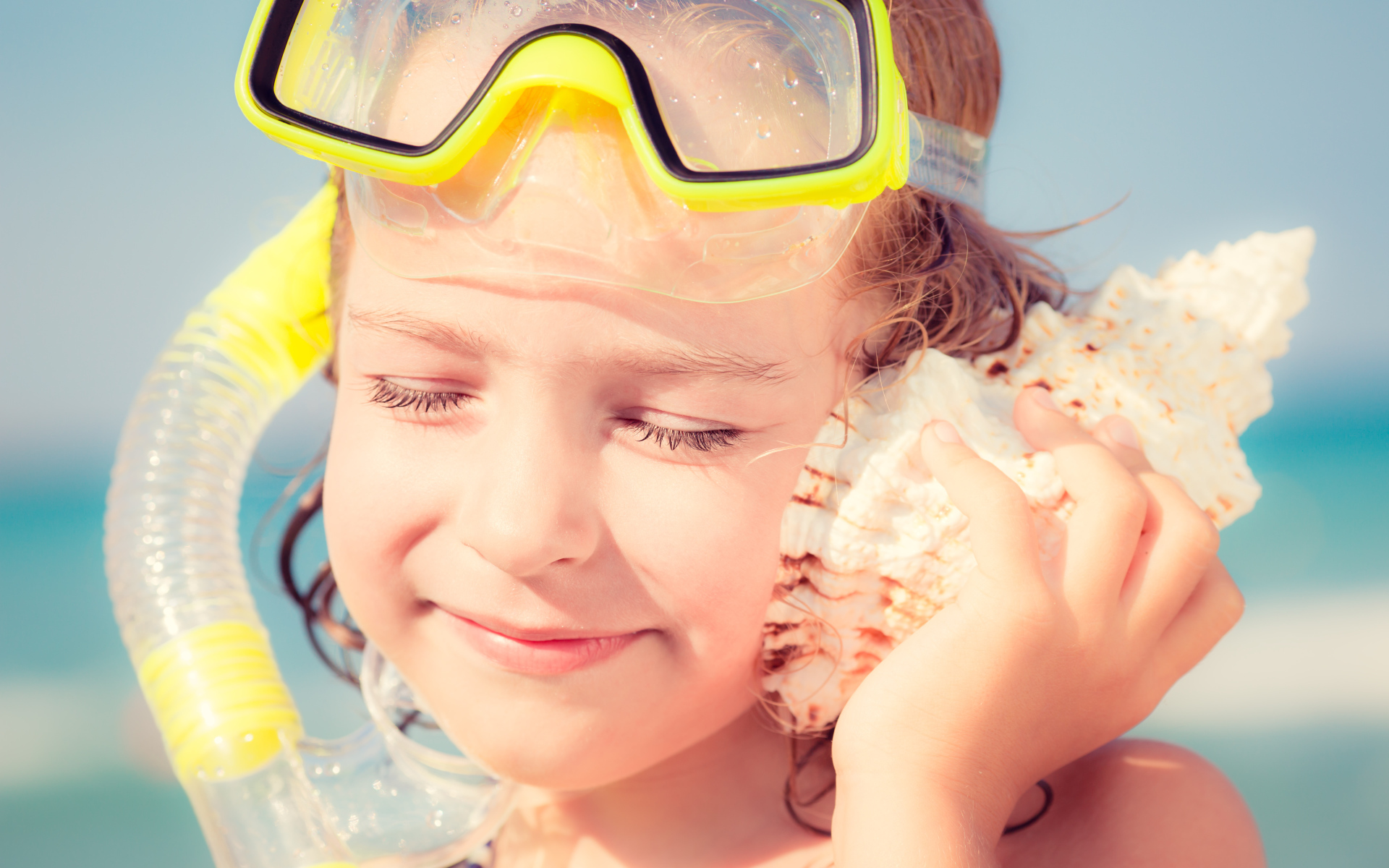 Маленькая девочка приложила ракушку к уху