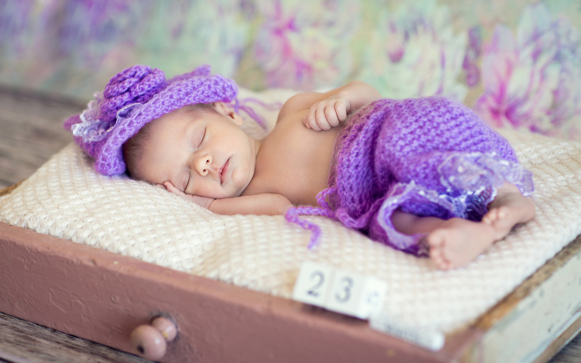 Маленький спящий младенец в вязаном фиолетовом костюме