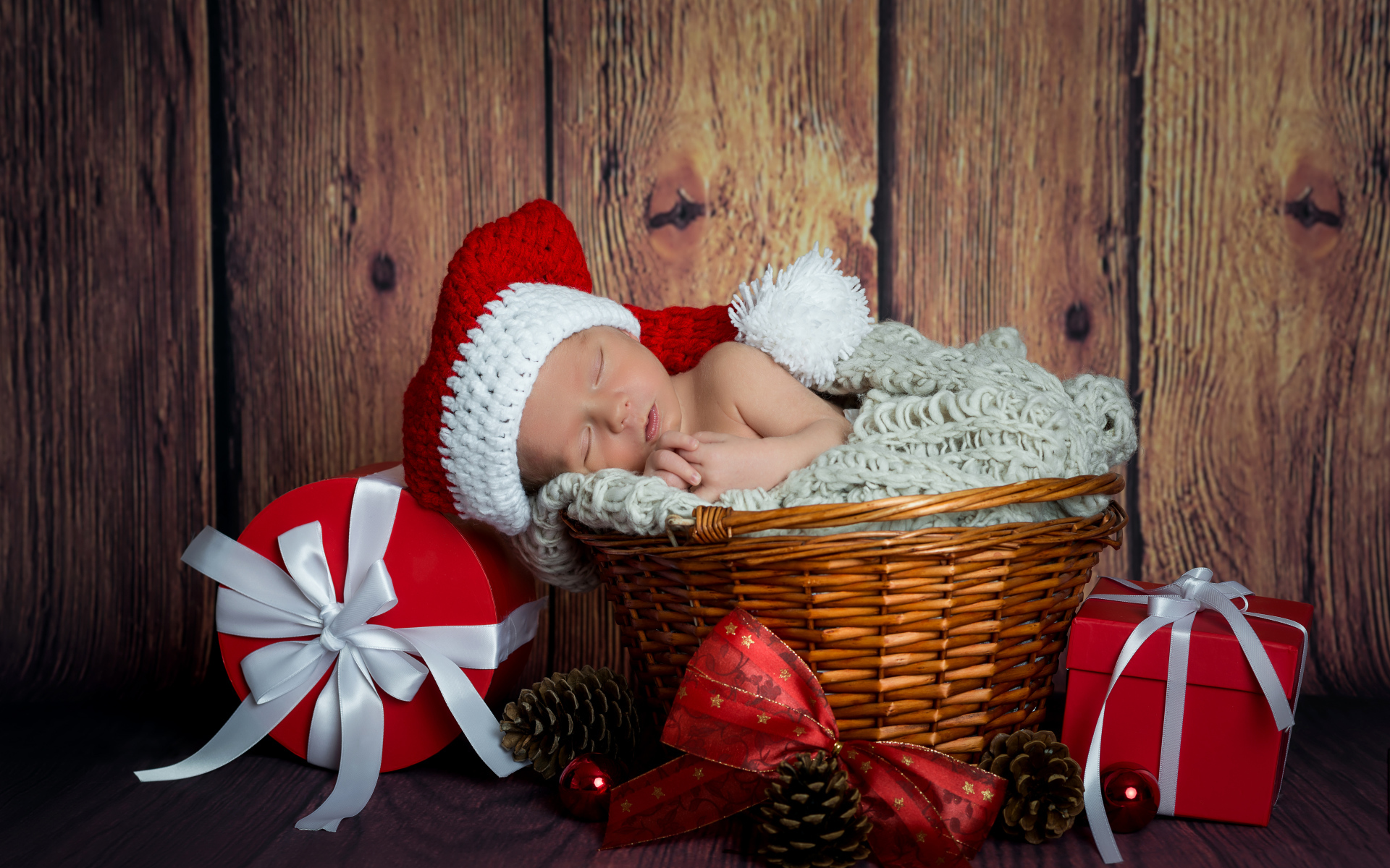 Маленький грудной ребенок спит в плетеной корзине с новогодними подарками