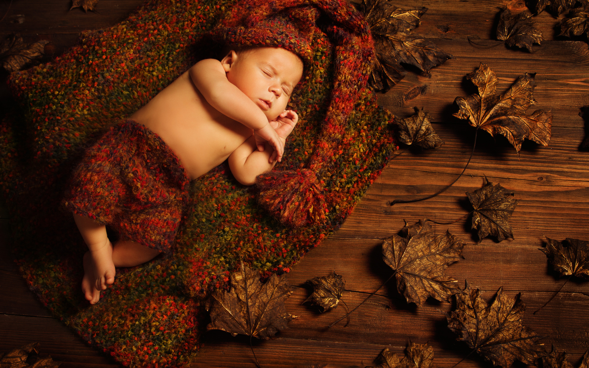 Маленький ребенок спит в вязаном костюме на полу с сухими листьями