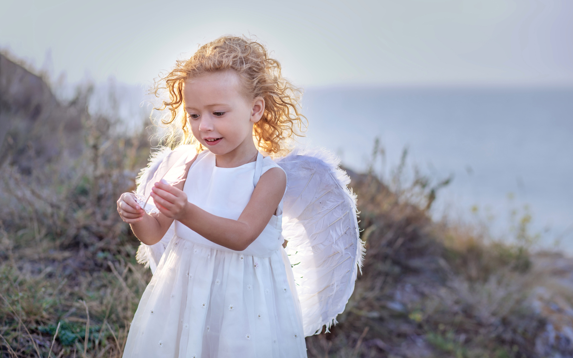 Красивая маленькая девочка в белом платье с крыльями ангела