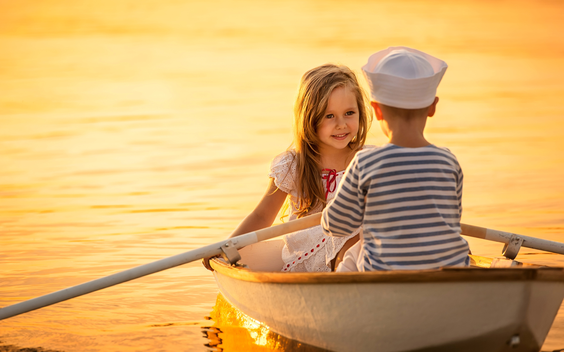 Маленькие мальчик и девочка плывут в лодке на закате солнца