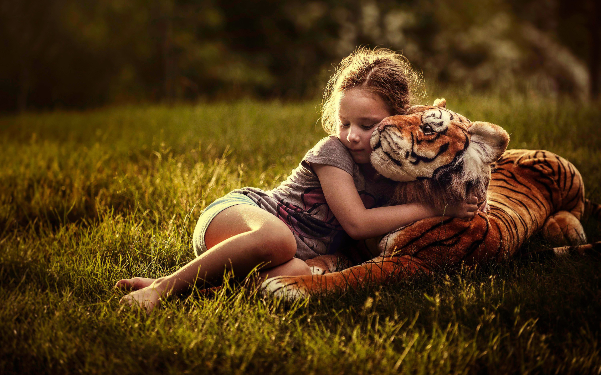 Маленькая девочка обнимает игрушечного тигра на зеленой траве