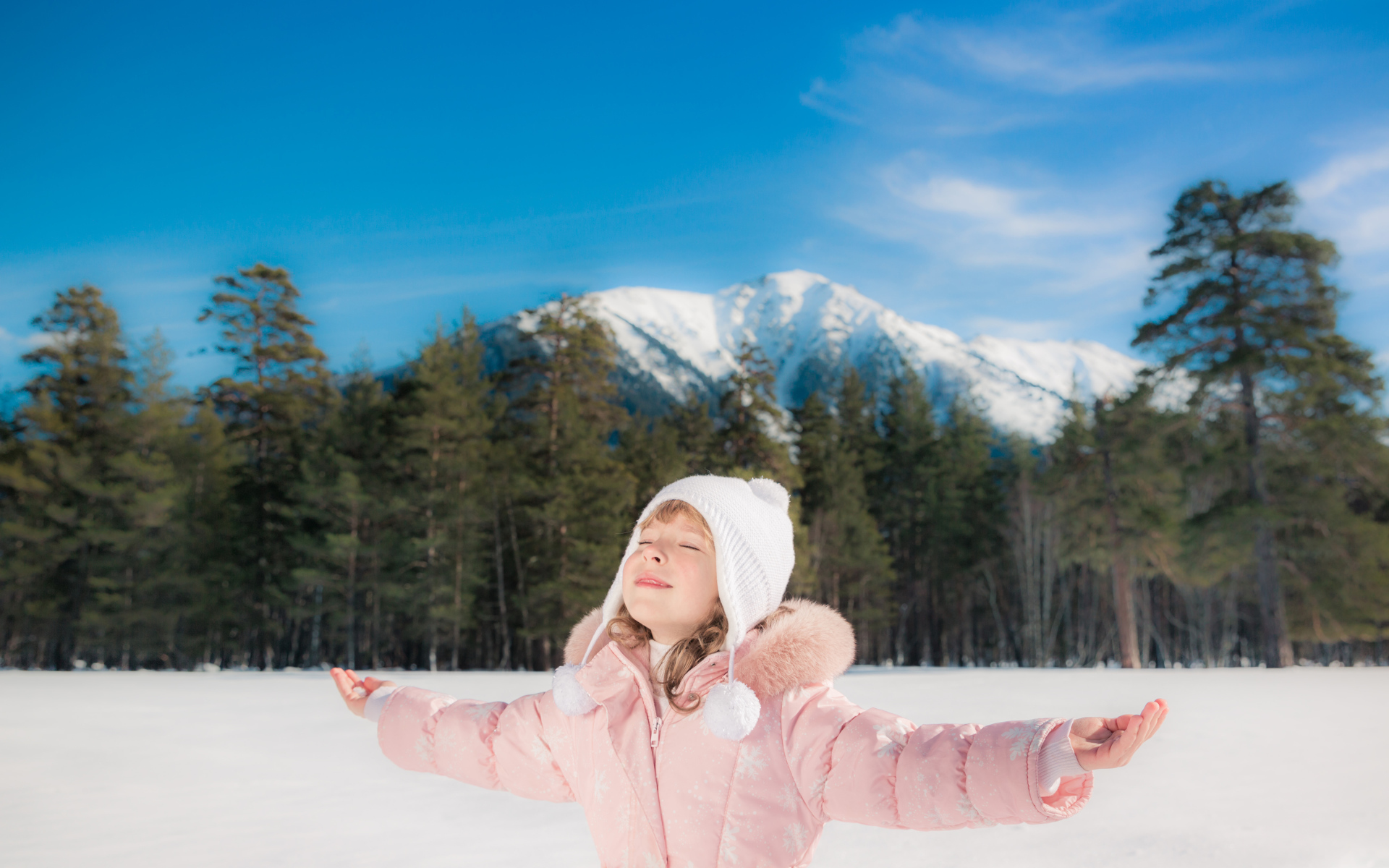 Маленькая девочка в розовой куртке на фоне гор зимой