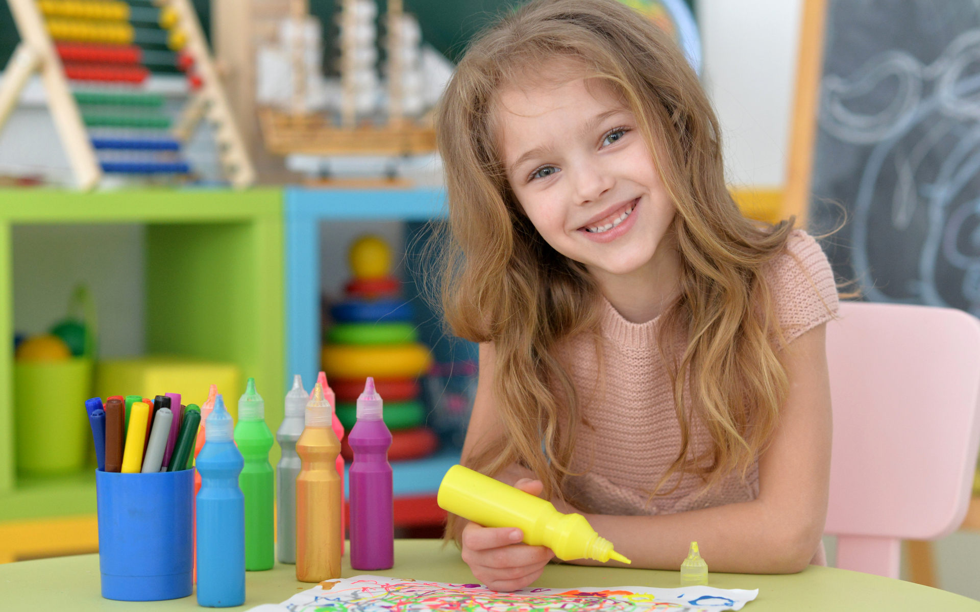 Маленькая улыбающаяся девочка рисует карандашами