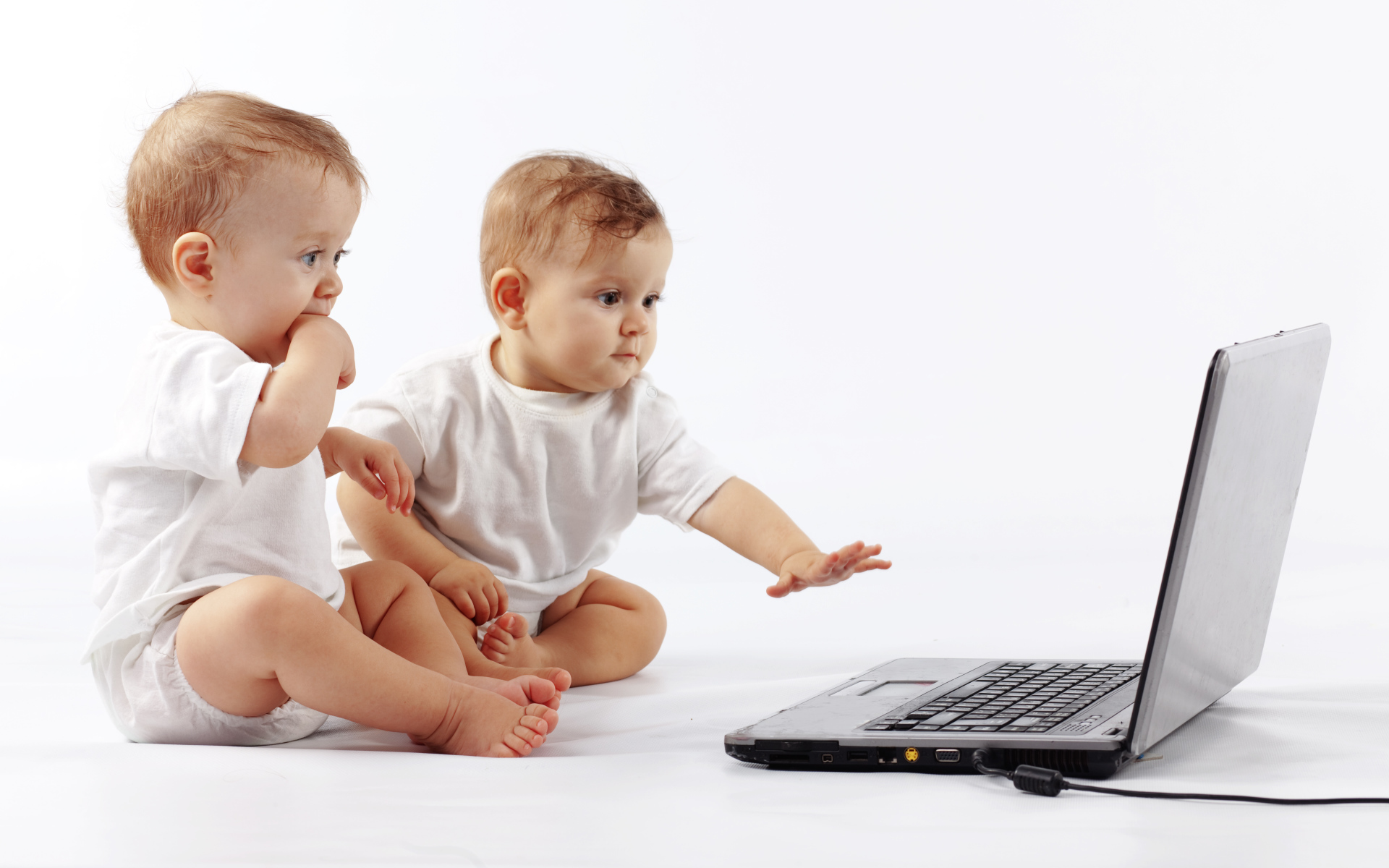 Два младенца перед ноутбуком на белом фоне