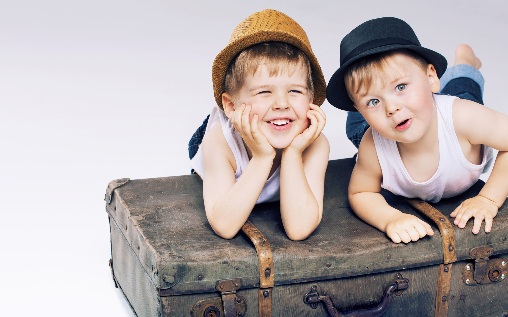 Два маленьких улыбающихся мальчика лежат на старом чемодане
