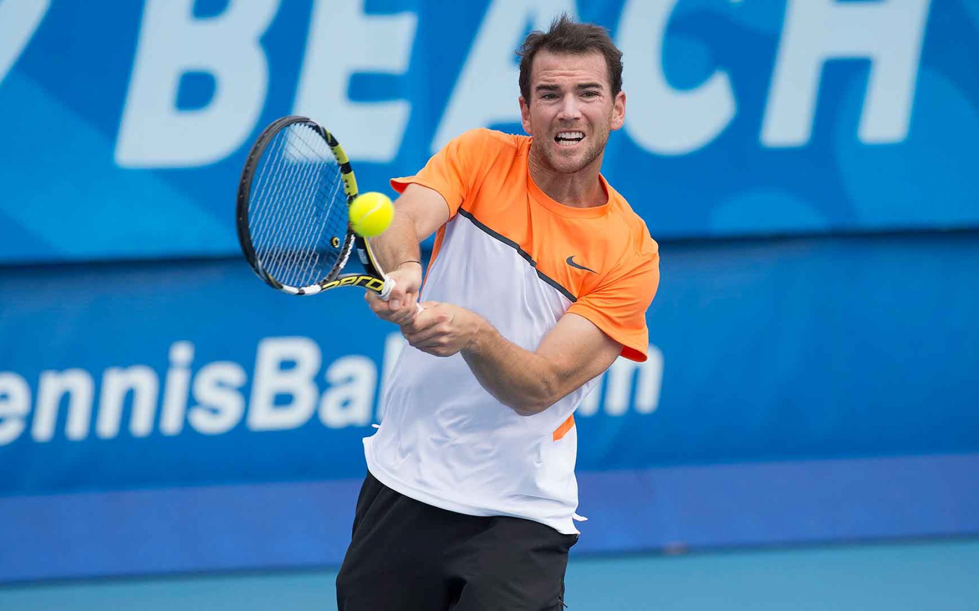 Теннисист Адриан Маннарино отбивает мяч ракеткой 