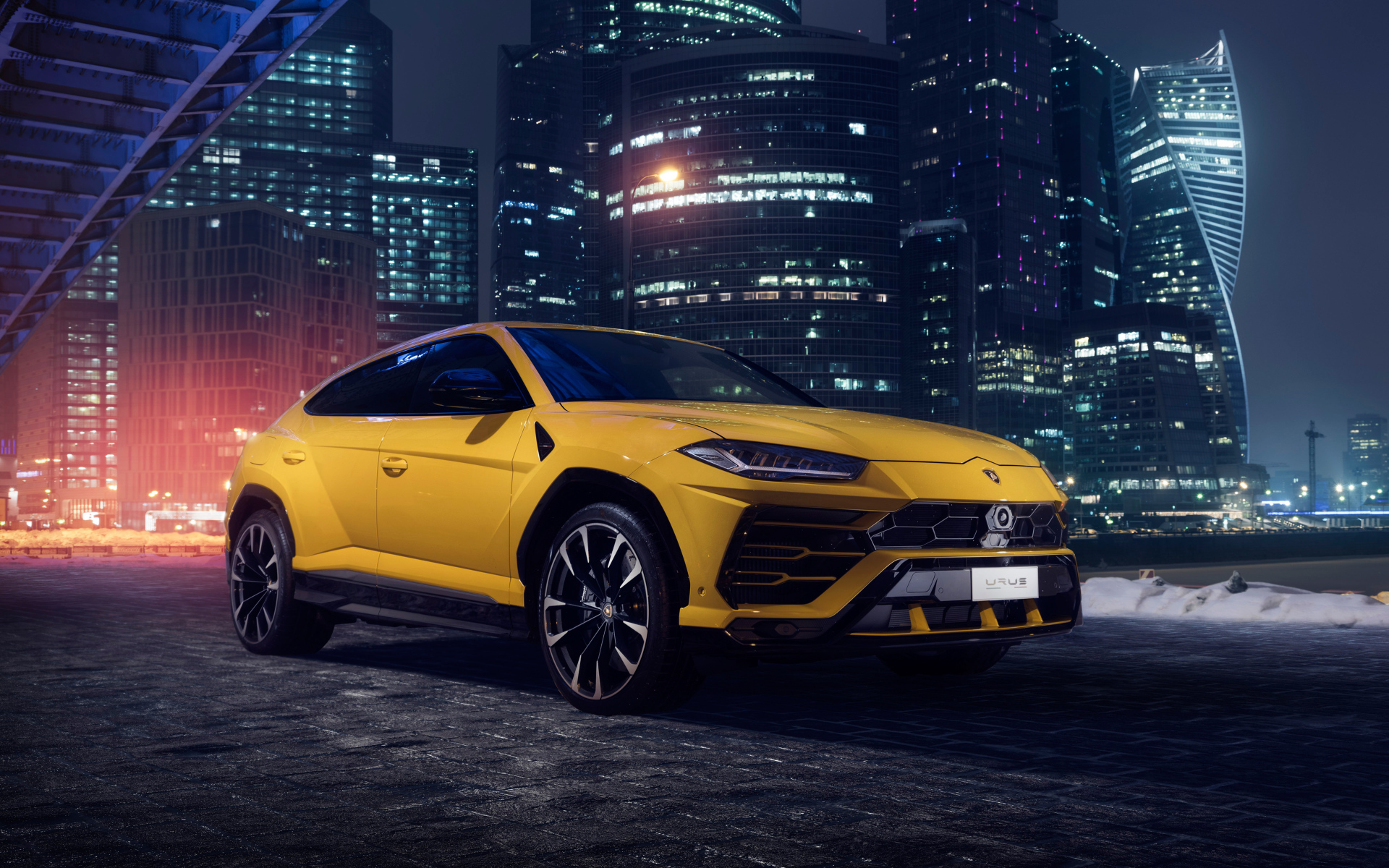 Желтый Lamborghini Urus на фоне ночных небоскребов