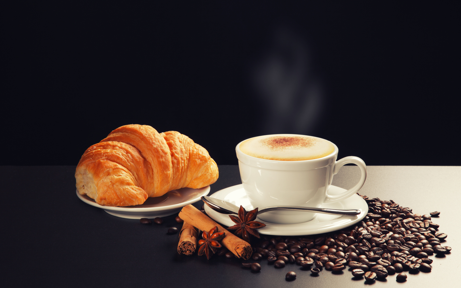 Чашка кофе на столе кофейными зернами, бадьяном, корицей  круассаном 