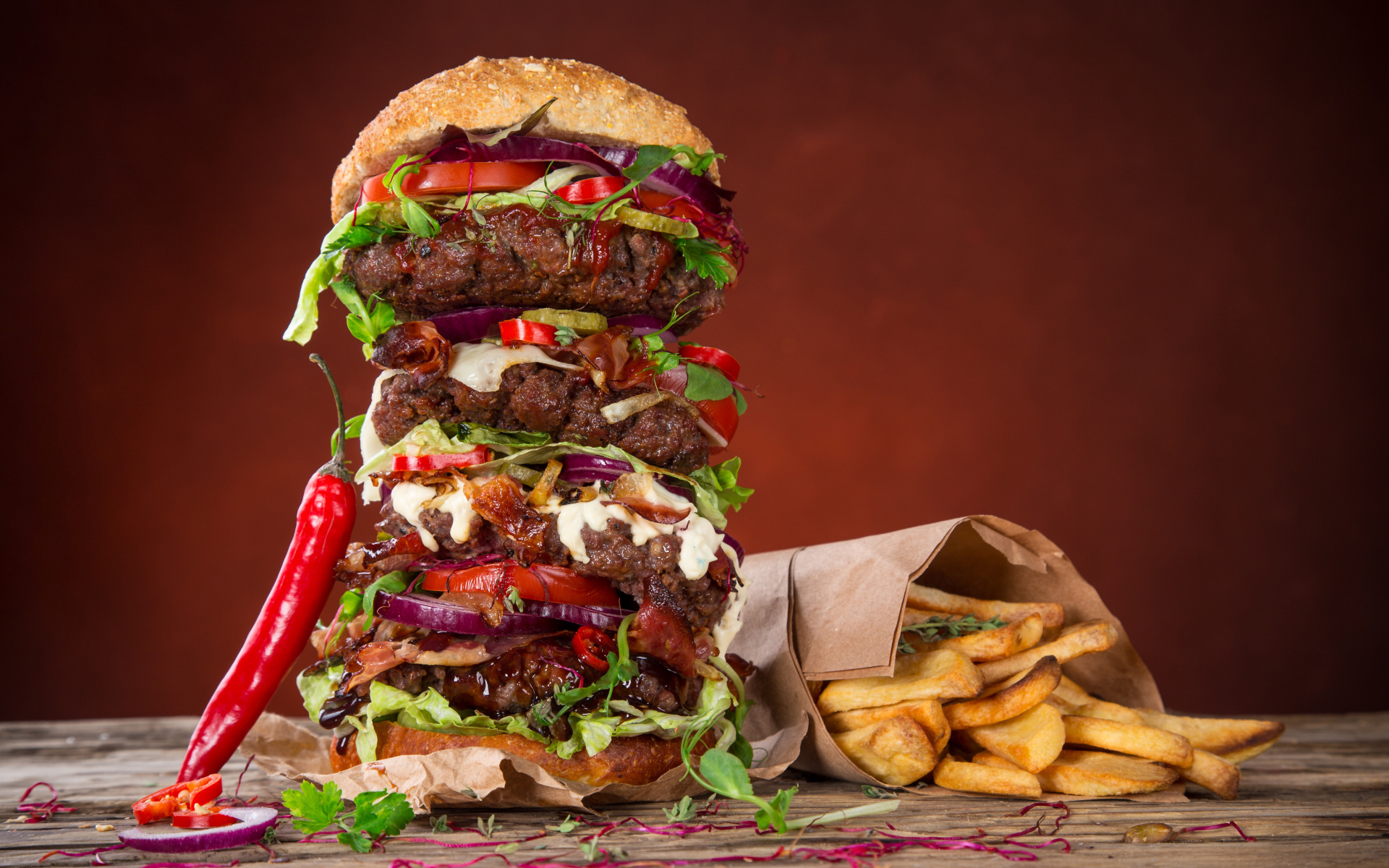 Огромный гамбургер на столе с картофелем фри и острым перцем