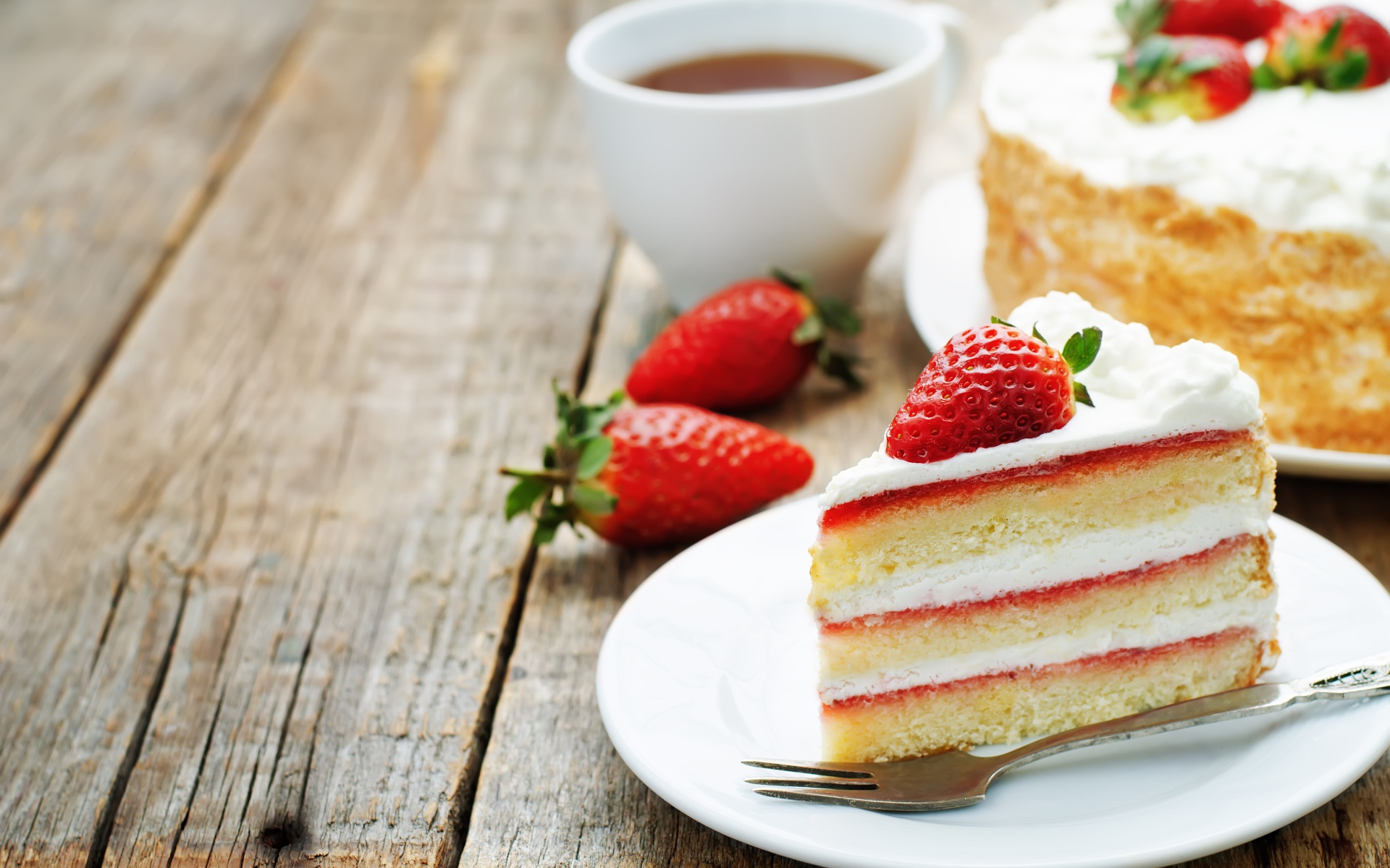 Кусок торта с клубникой на столе с чашкой чая 