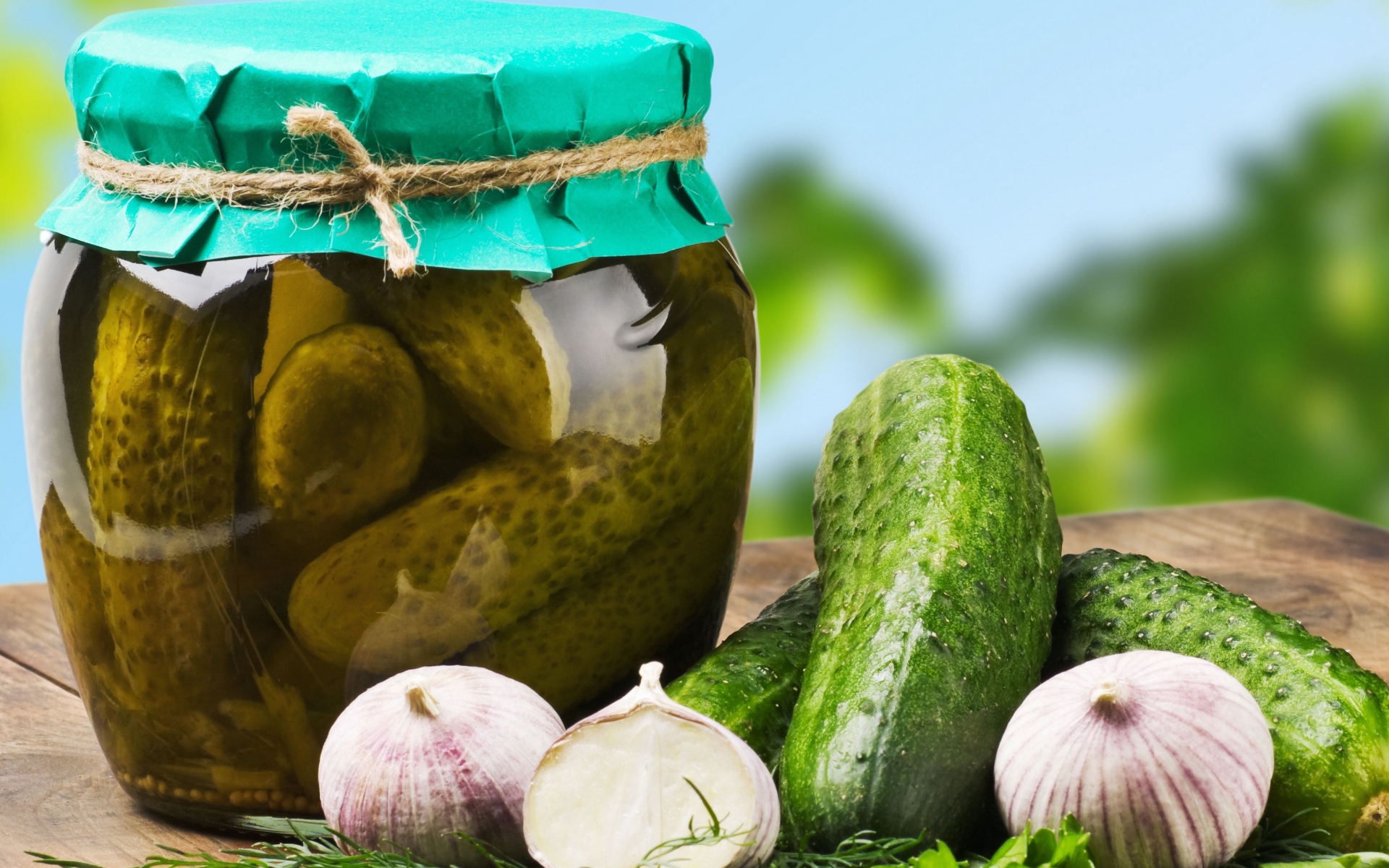 Консервированные огурцы в банке на столе со свежими огурцами и чесноком