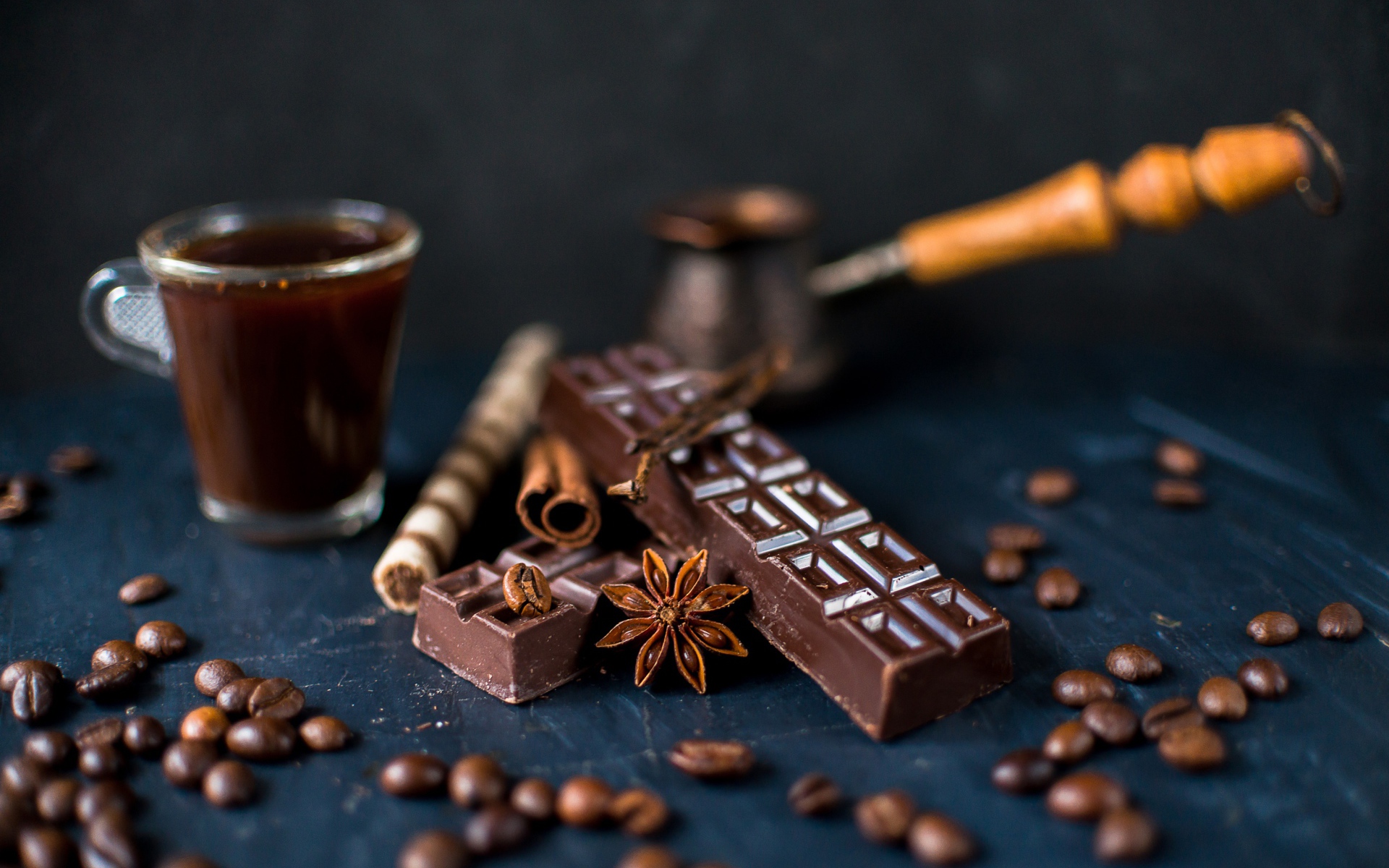 A cup of coffee on a table with chocolate and coffee beans