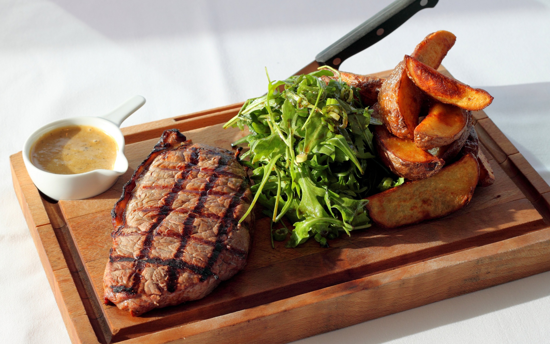 Стейк на доске с картофелем, соусом и рукколой