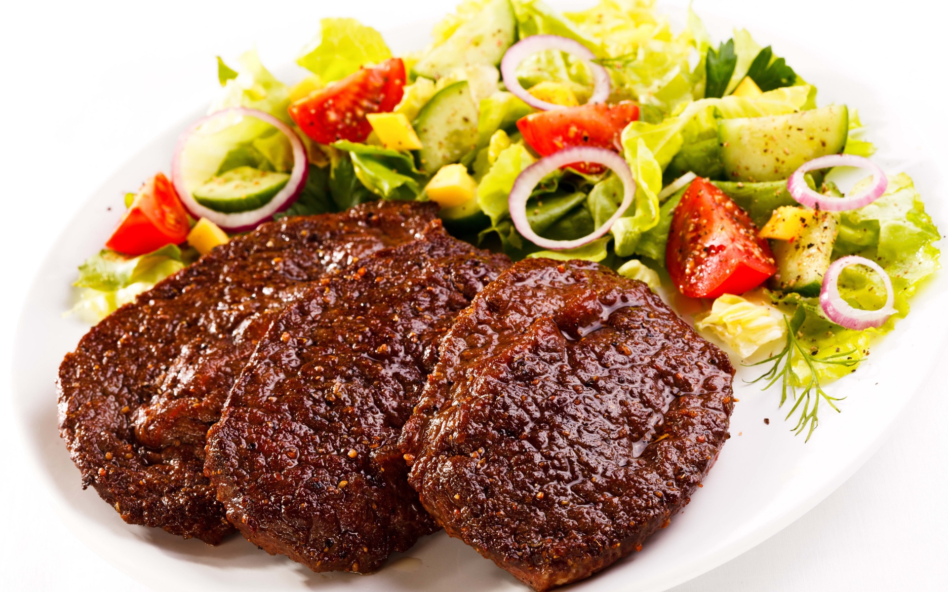 Три котлеты на тарелке с салатом на белом фоне