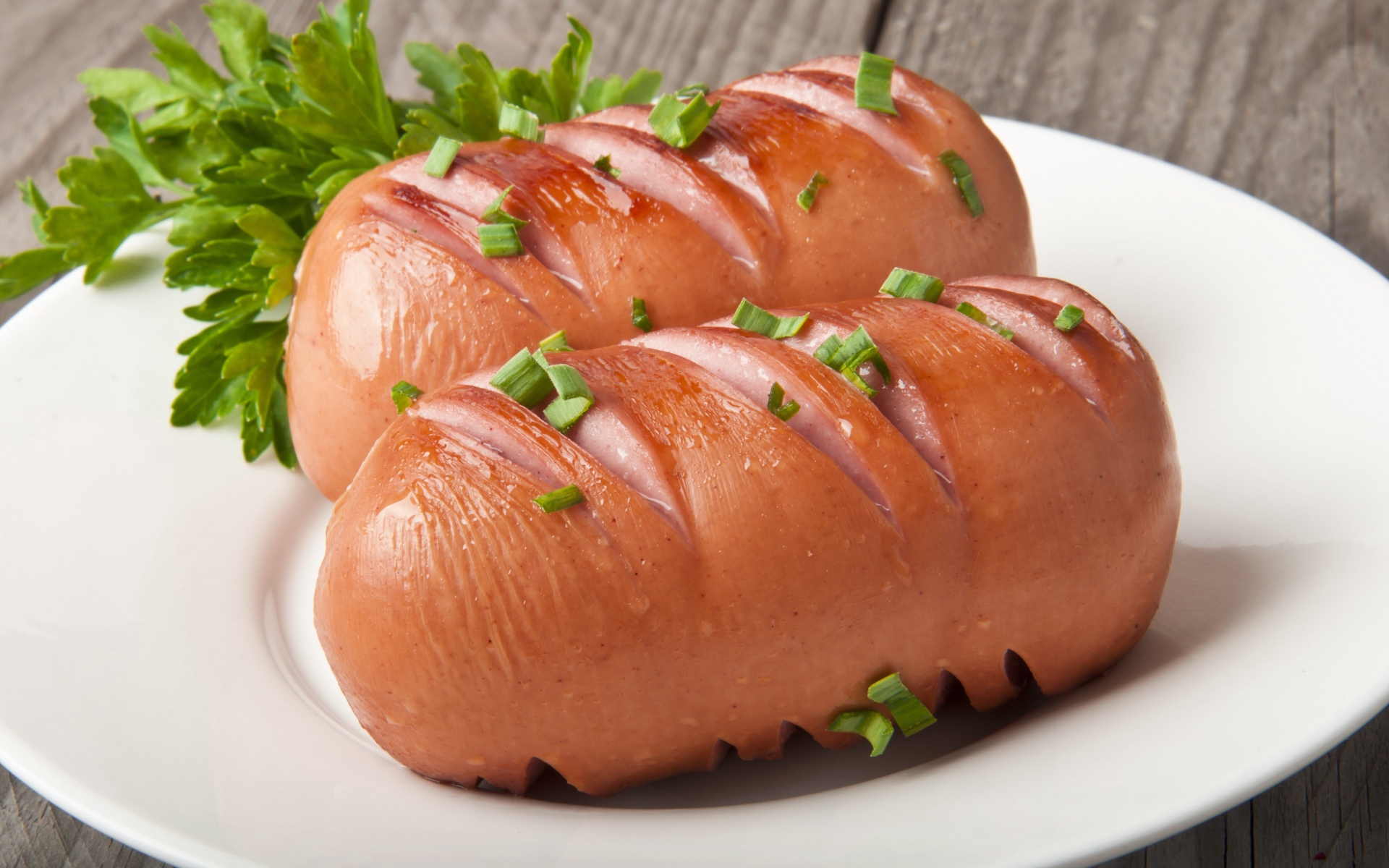 Два жареные сардельки на большой белой тарелке с зеленью 