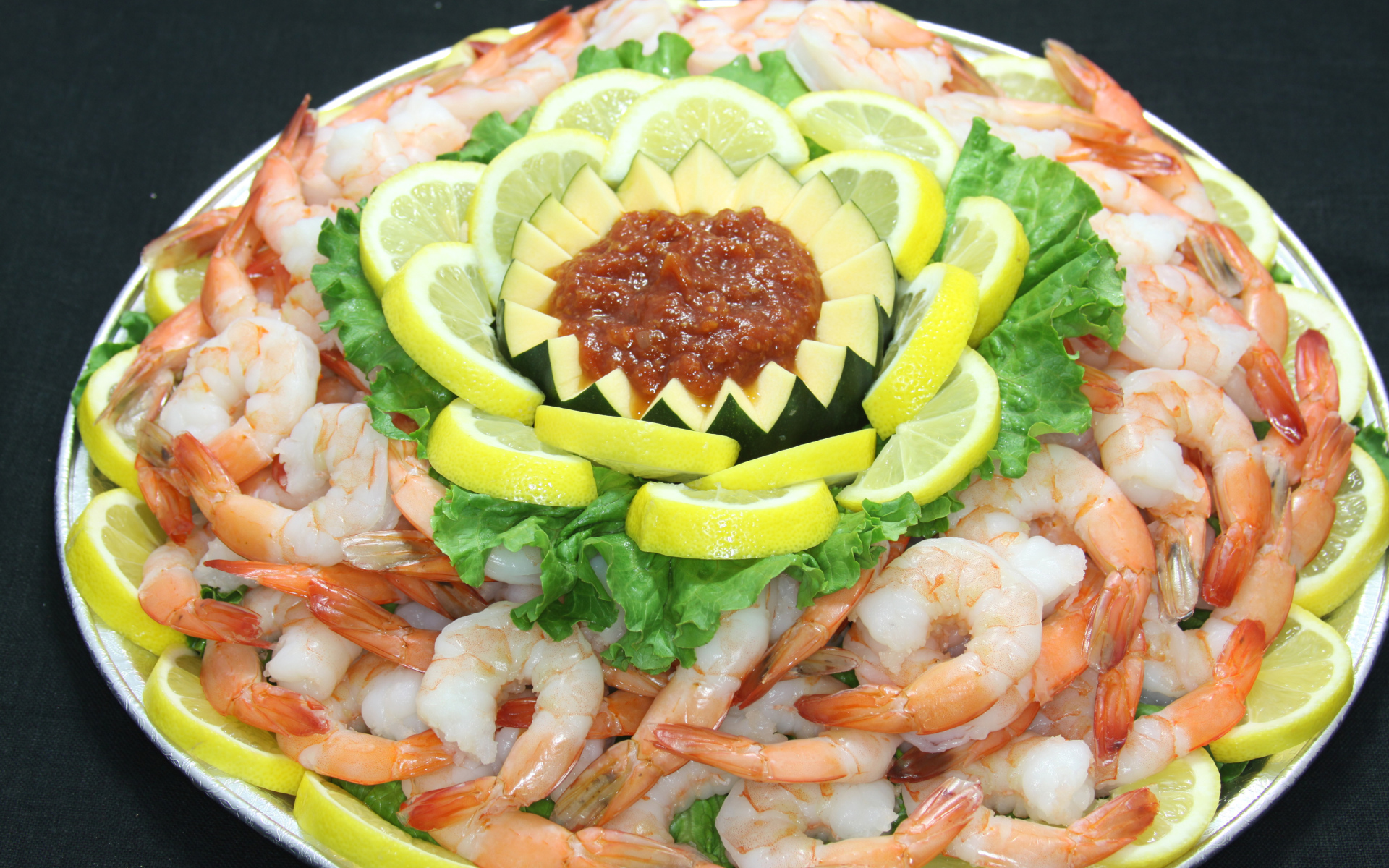 Вареные креветки с лимоном и соусом на большой тарелке