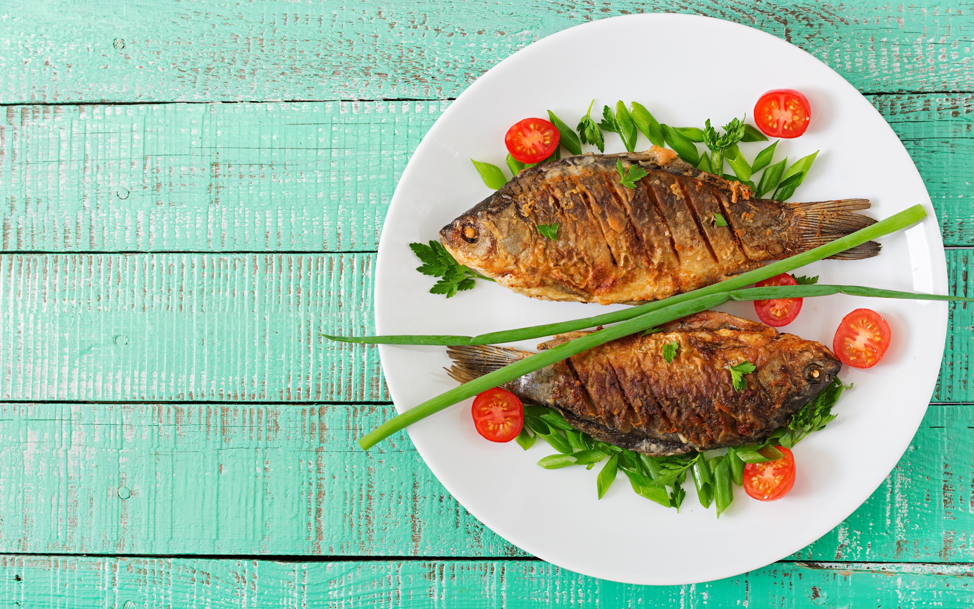 Жареная рыба с помидорами и зеленью на столе