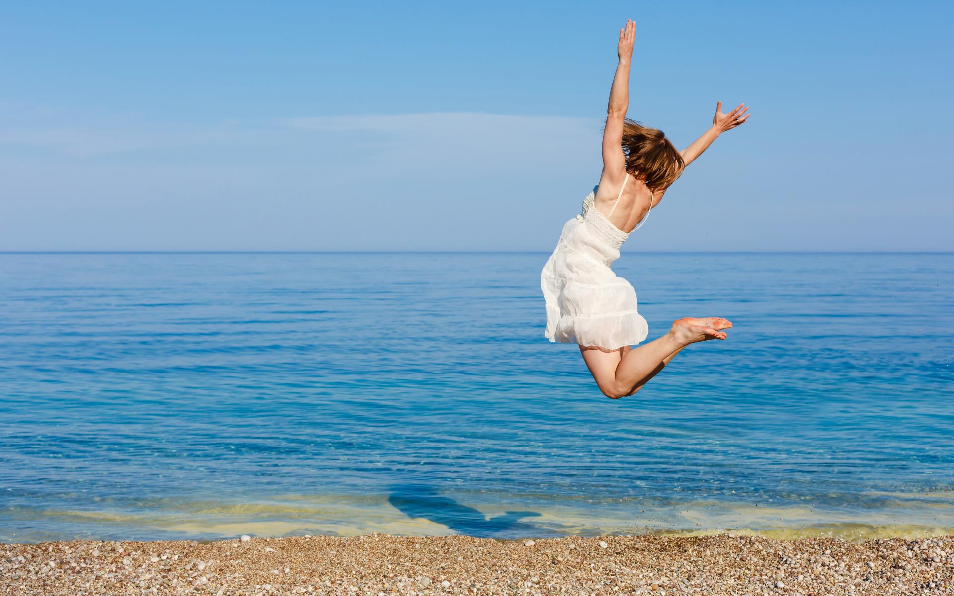 Молодая девушка в белом платье делаем прыжок на песке у моря