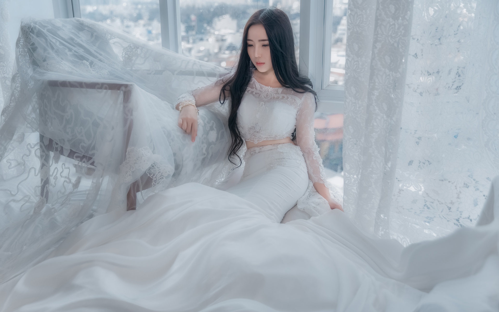 Красивая азиатка в белом свадебном платье сидит на полу