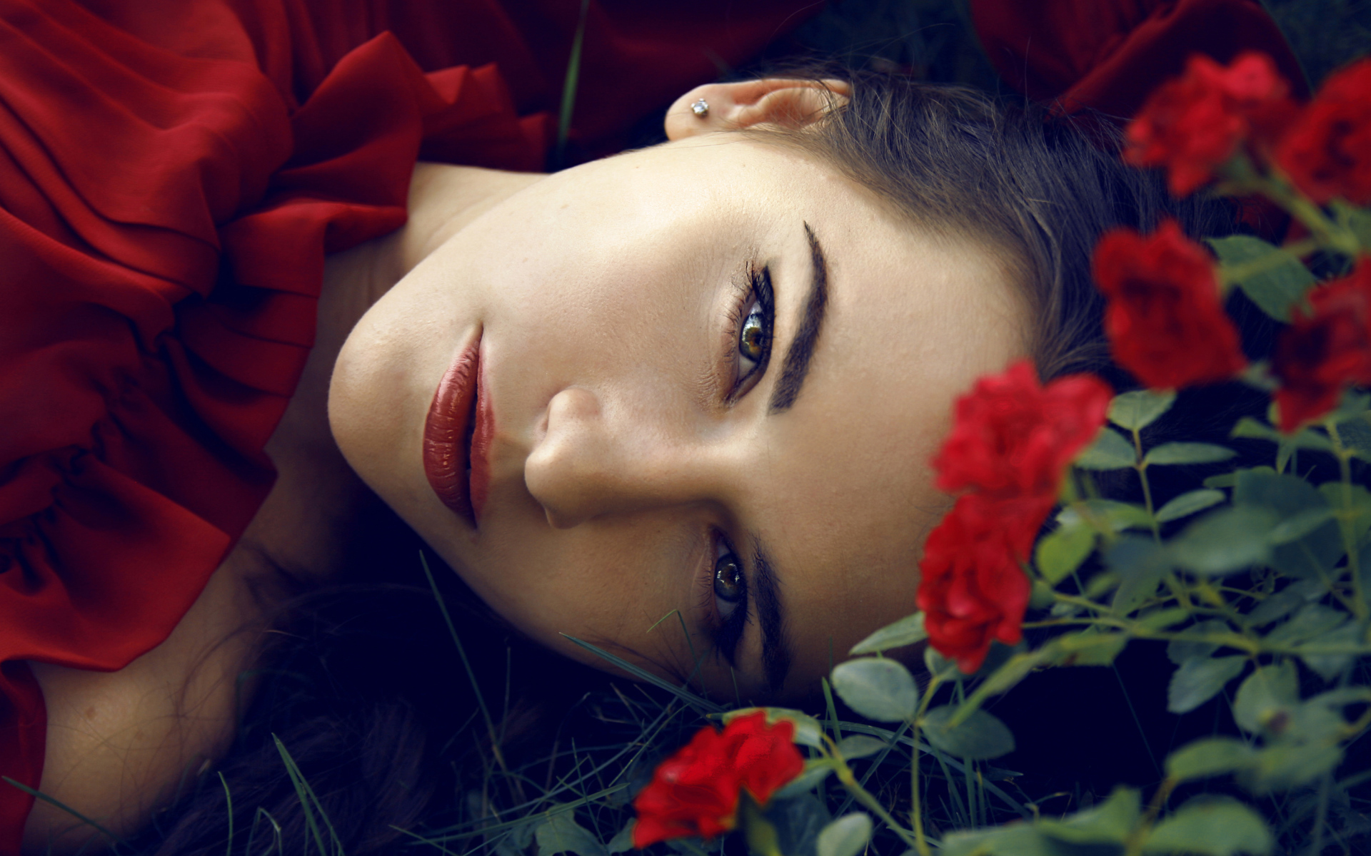 Красивая брюнетка лежит на траве с красными розами