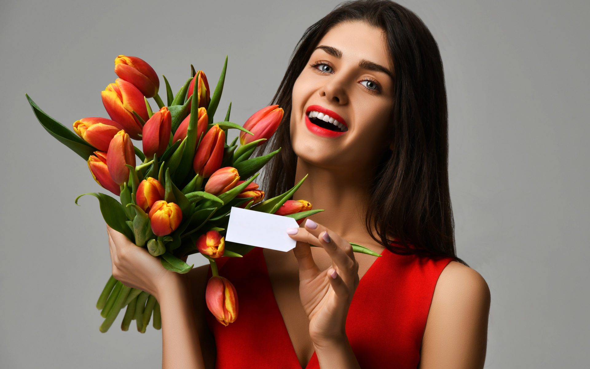 Красивая брюнетка с букетом тюльпанов на сером фоне