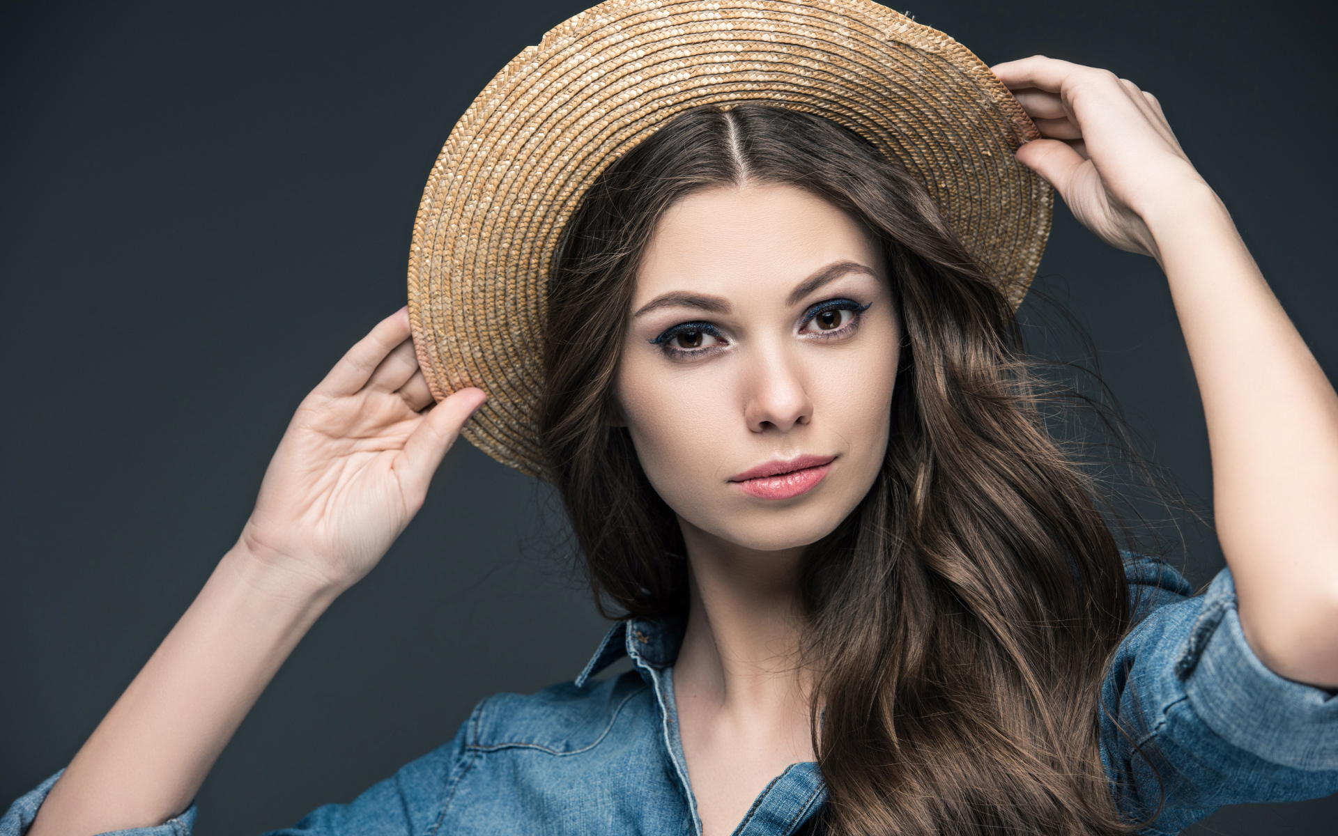 Красивая девушка в соломенной шляпе на сером фоне