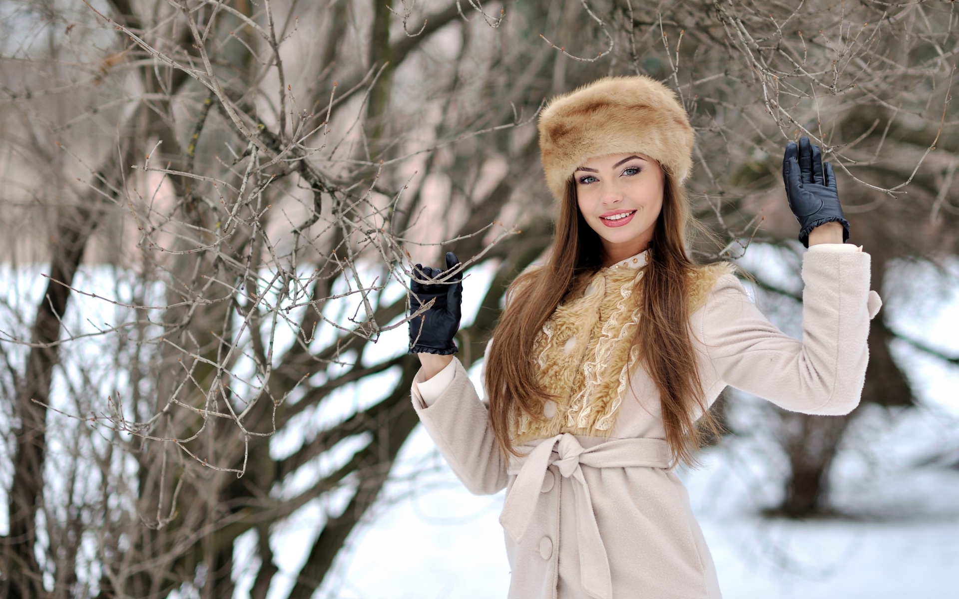 Красивая улыбающаяся девушка в шапке у дерева зимой