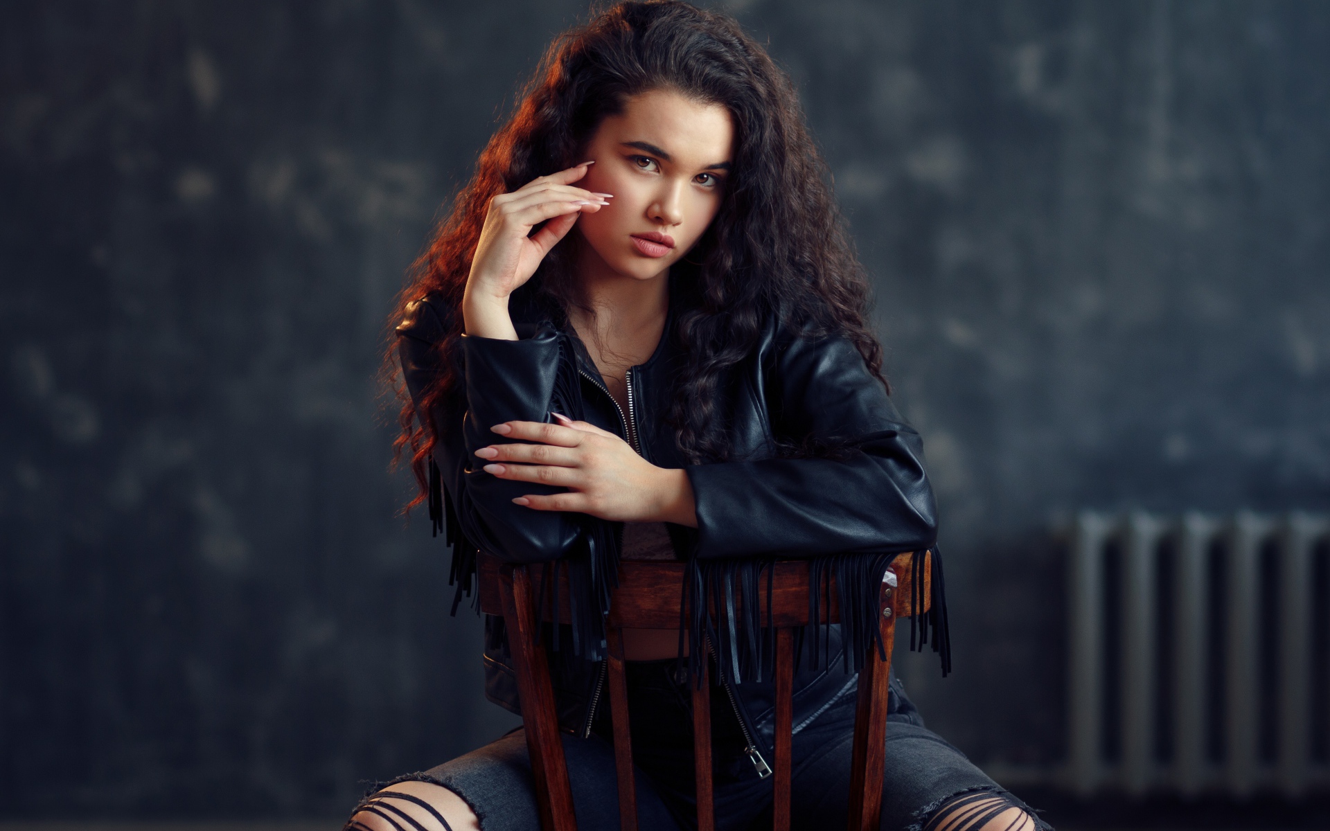 Модная красивая девушка в черное кожаной куртке сидит на стуле