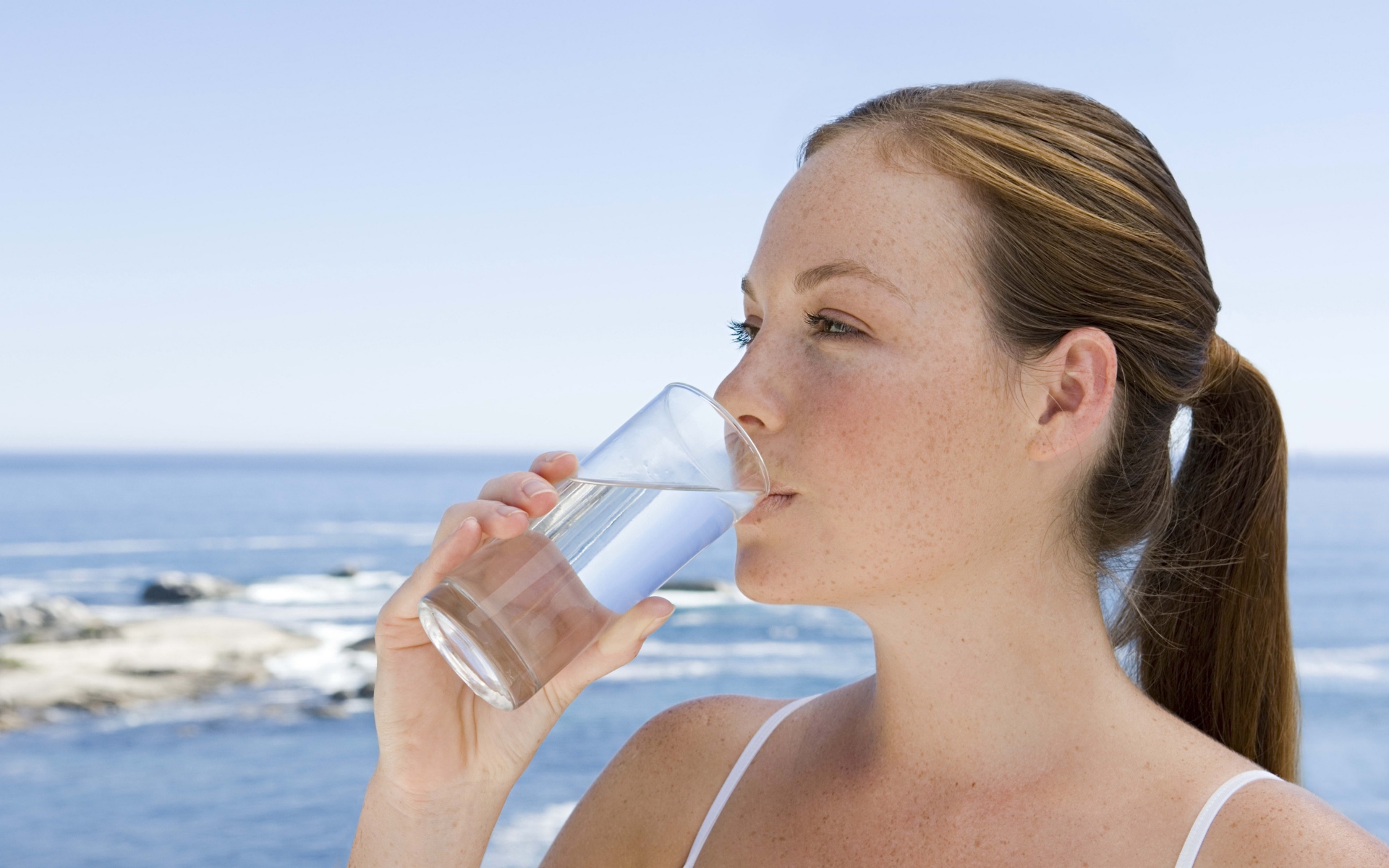 Девушка пьет воду со стакана на фоне моря