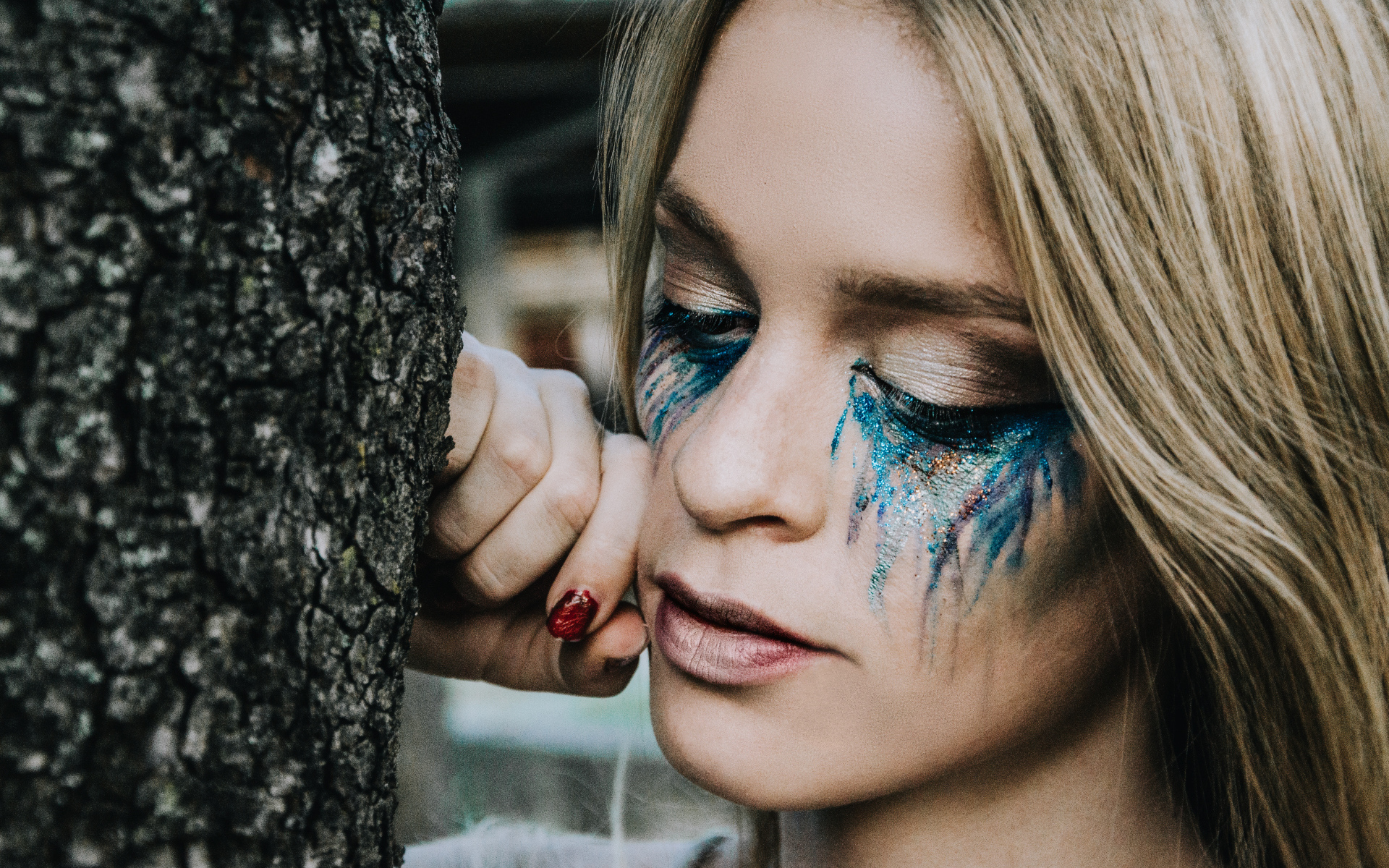 Заплаканная блондинка стоит у дерева