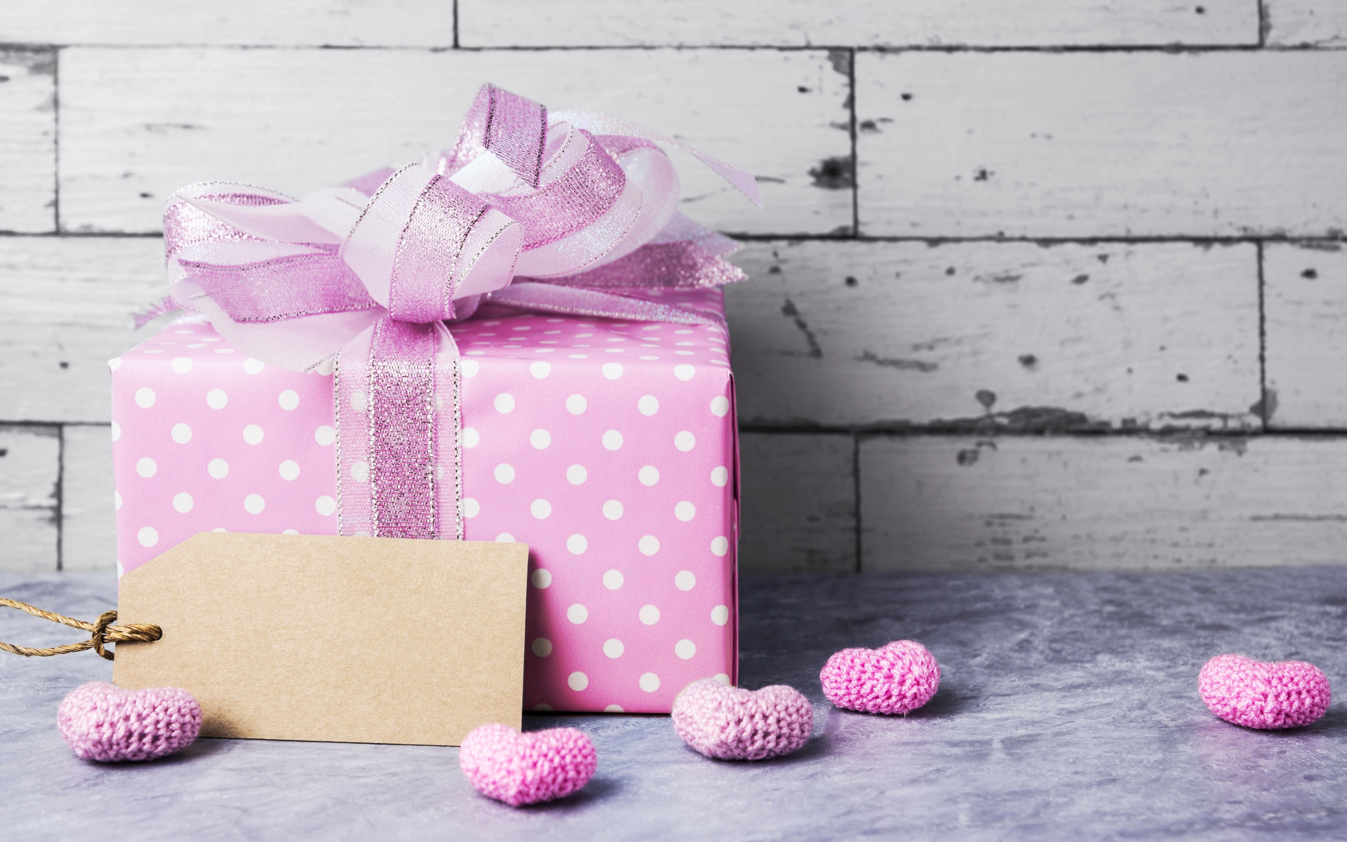 Large lilac gift box with a bow and small hearts against the wall