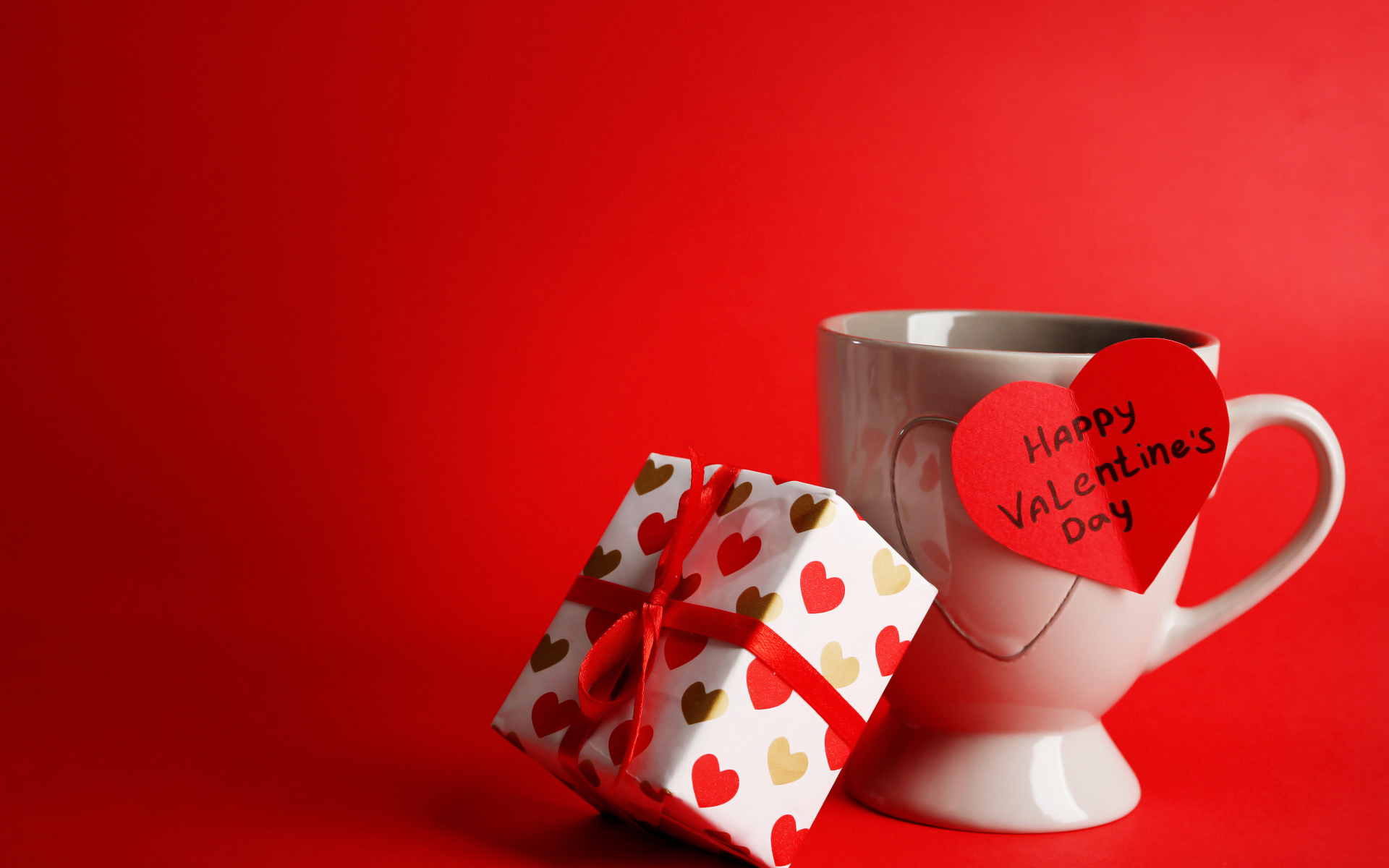 Чашка с подарком и валентинкой на красном фоне на 14 февраля