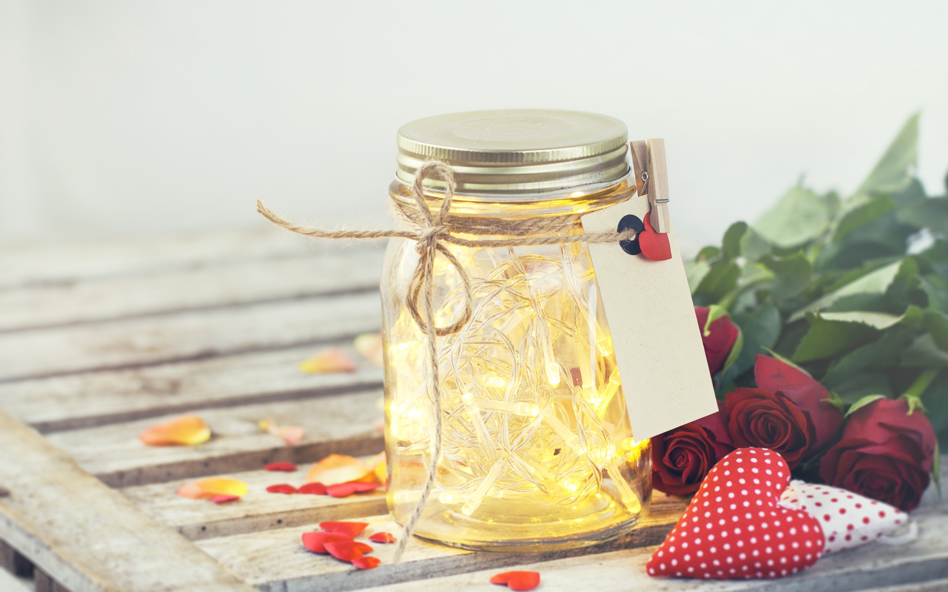 Стеклянная банка с гирляндой на столе с букетом роз и сердечками