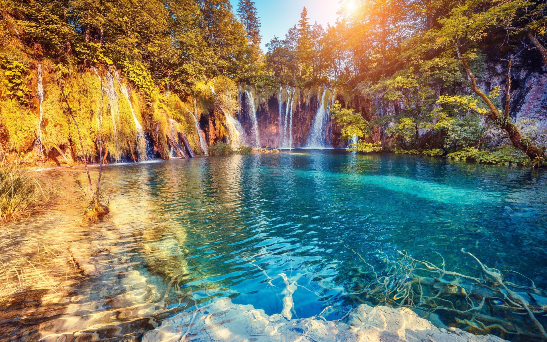 Водопад в лучах солнца стекает со скалы в реку